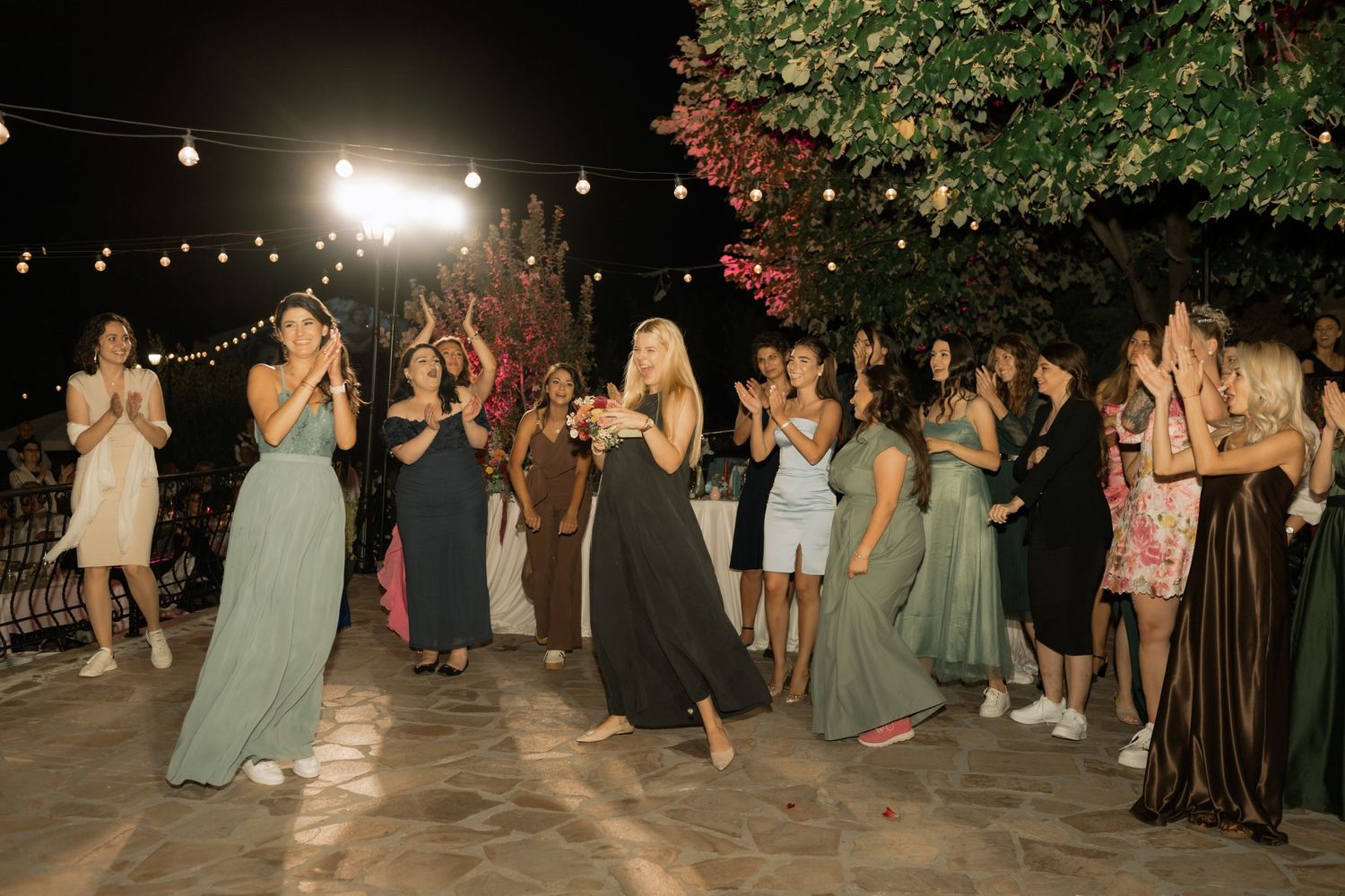 Wedding guests dancing together on an outdoor dance floor at night under string lights and trees.