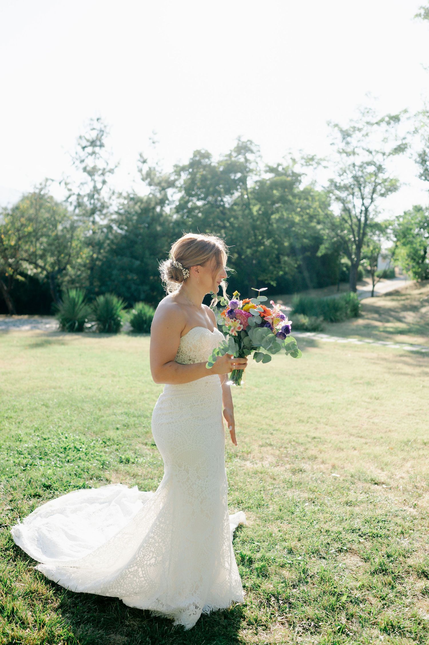 Person in strapless wedding gown poses with colorful bouquet in an outdoor setting.