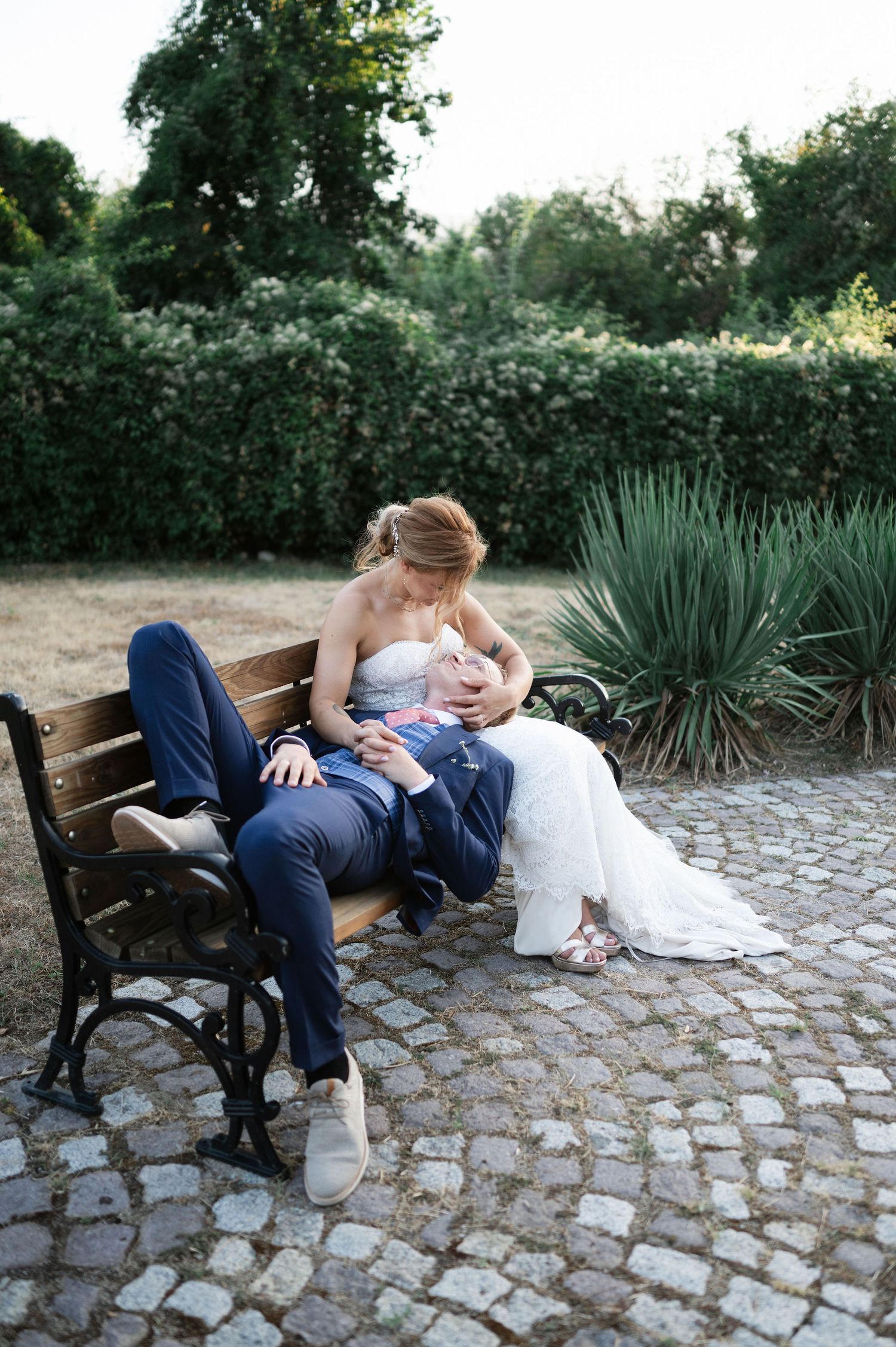 Wedding couple shares intimate moments on a cobblestone path with decorative bench and greenery.