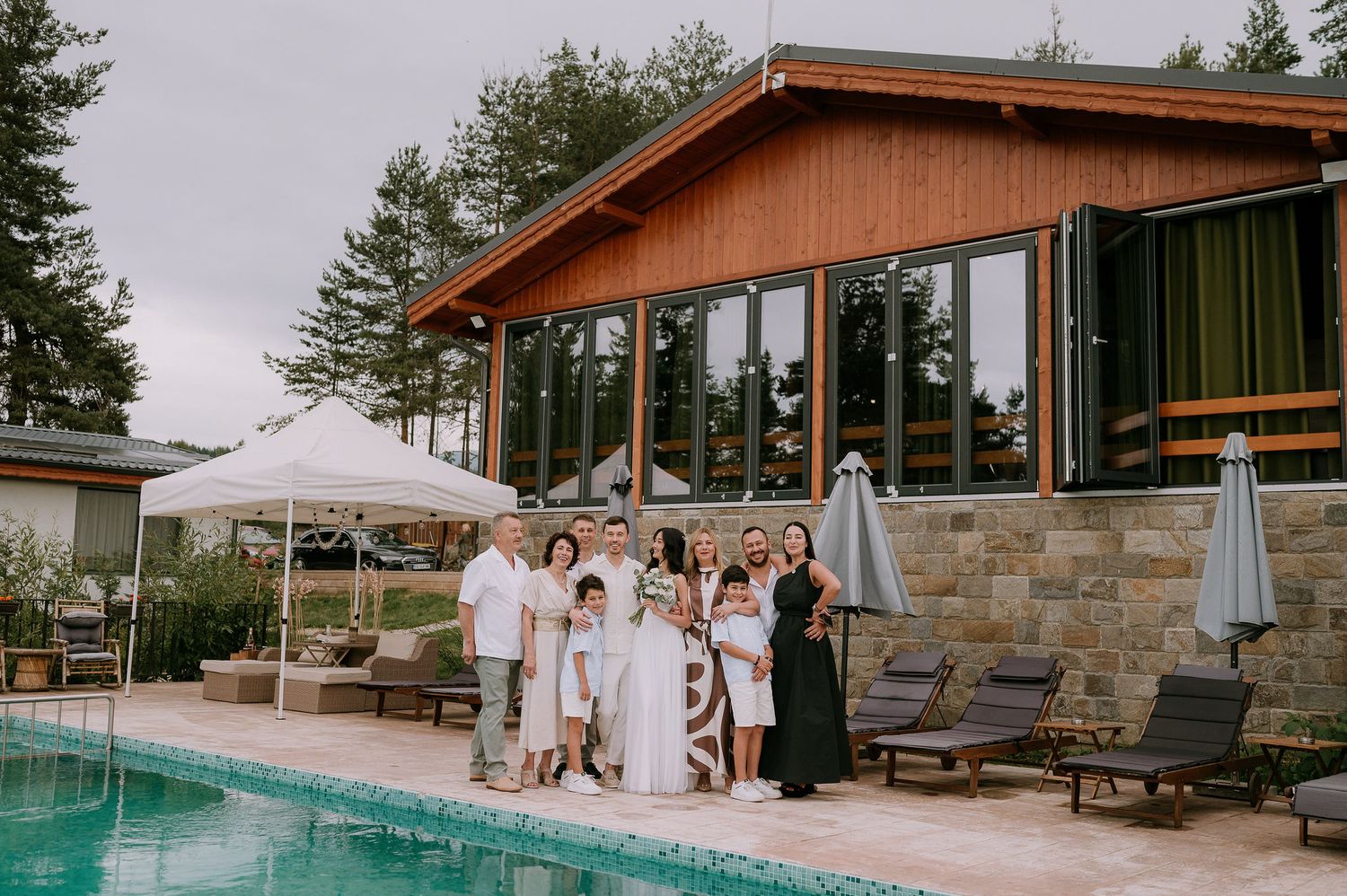 Elegant outdoor wedding ceremony setup with wooden arch and pool deck in a scenic mountain setting.