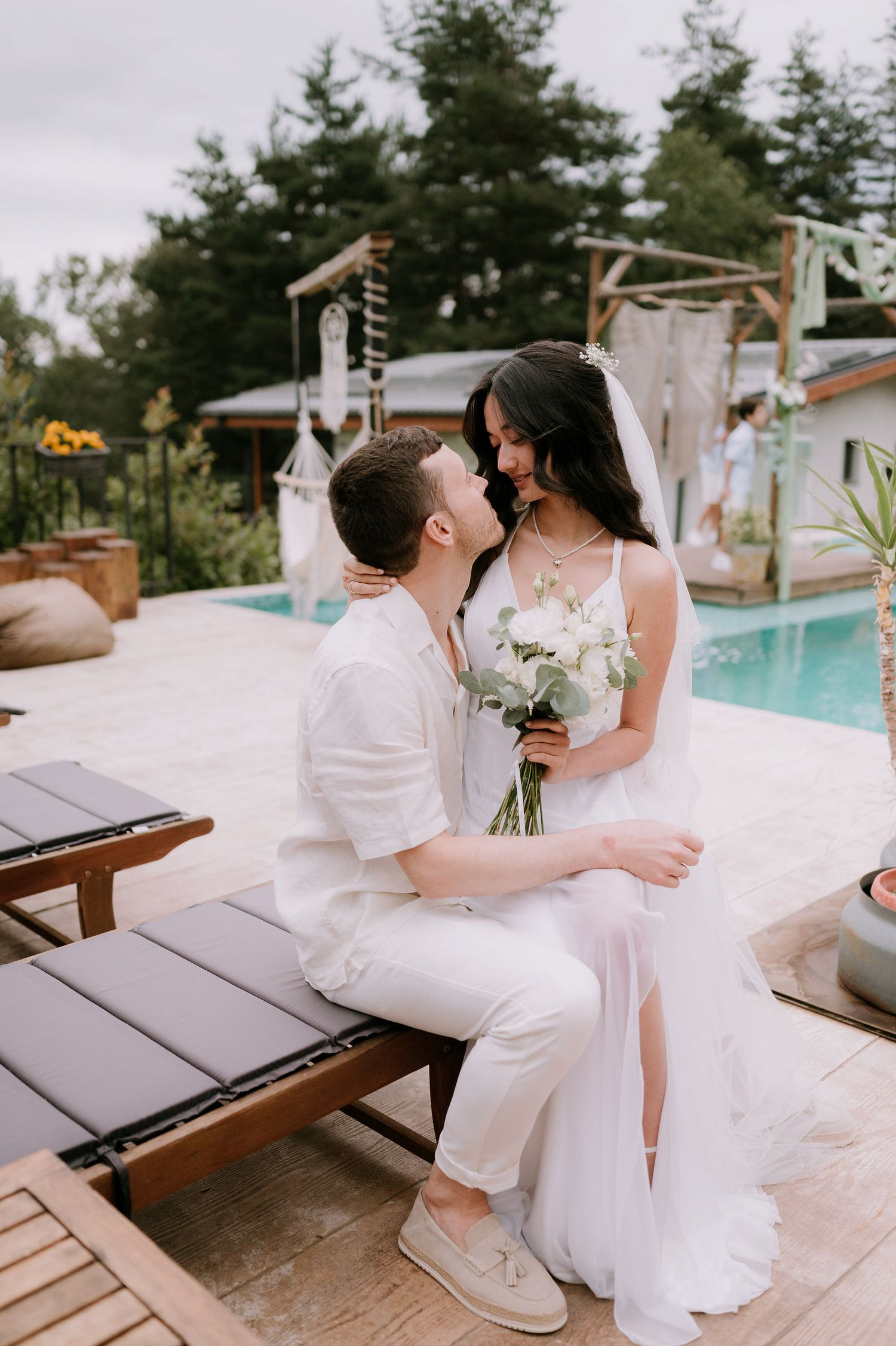Intimate wedding photography session by pool with couple in matching white outfits.