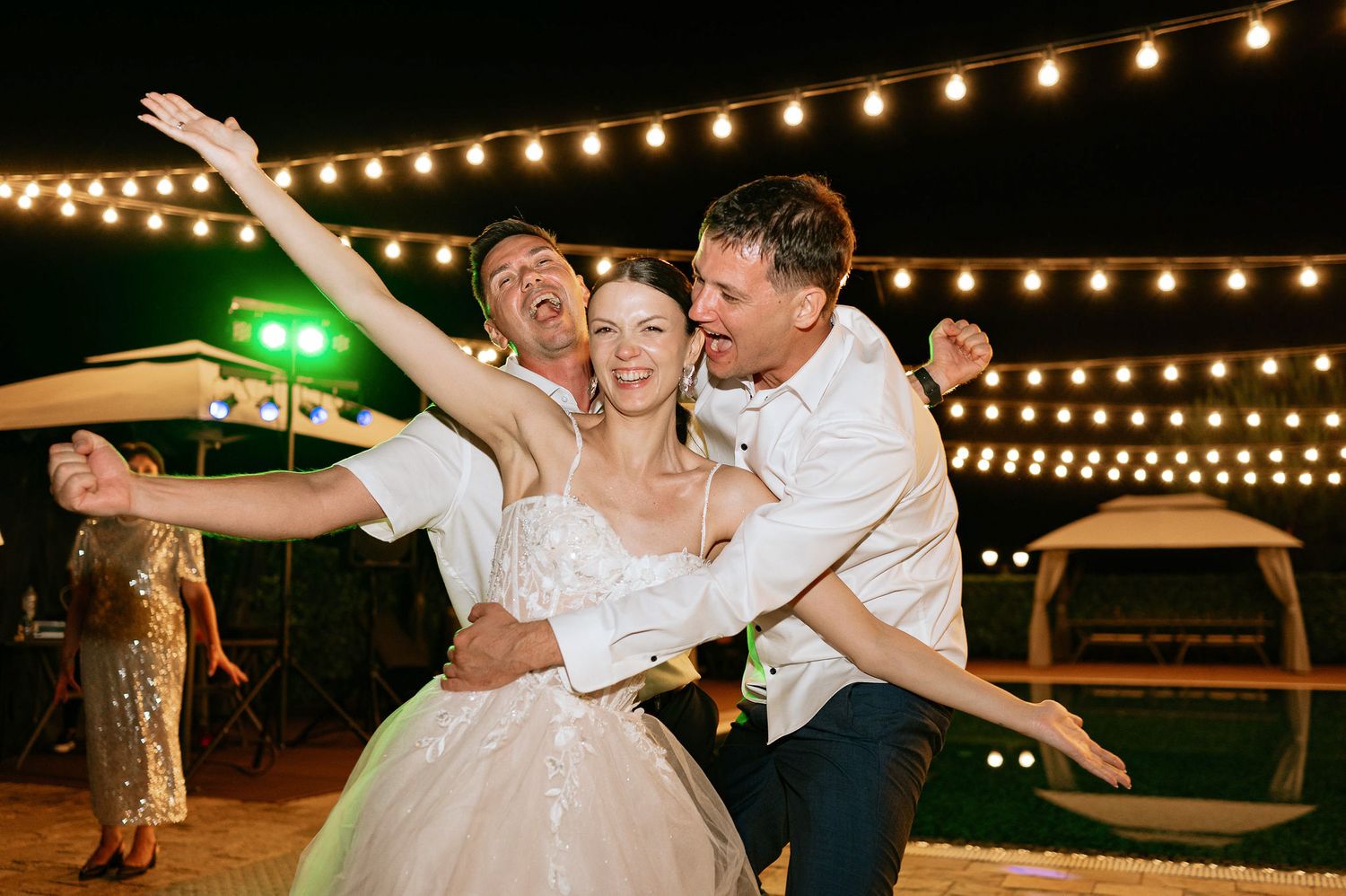 Wedding couple dances joyfully under twinkling outdoor lights during their reception celebration.
