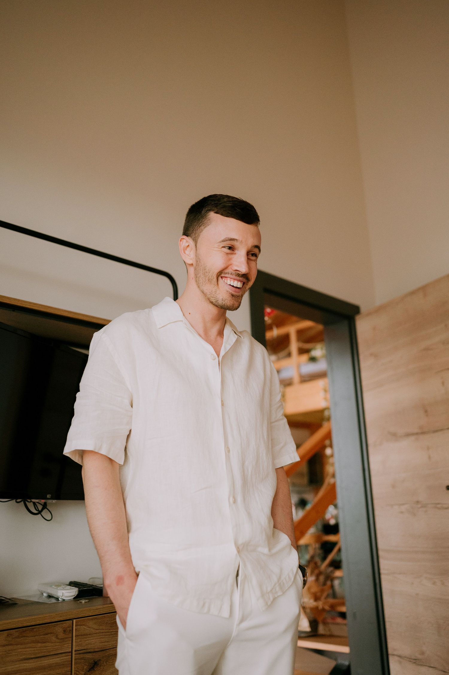 Person in all-white outfit sitting casually in modern interior setting.