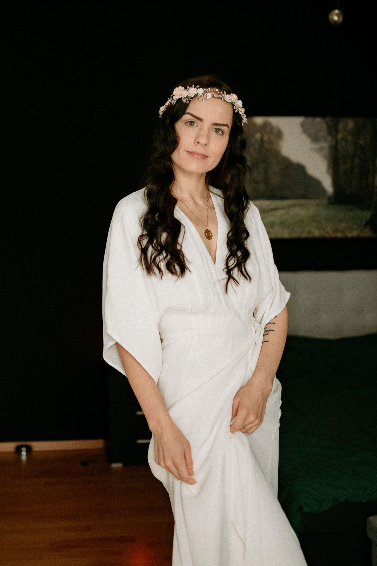 Person wearing a white robe and floral crown in a series of artistic indoor portraits.