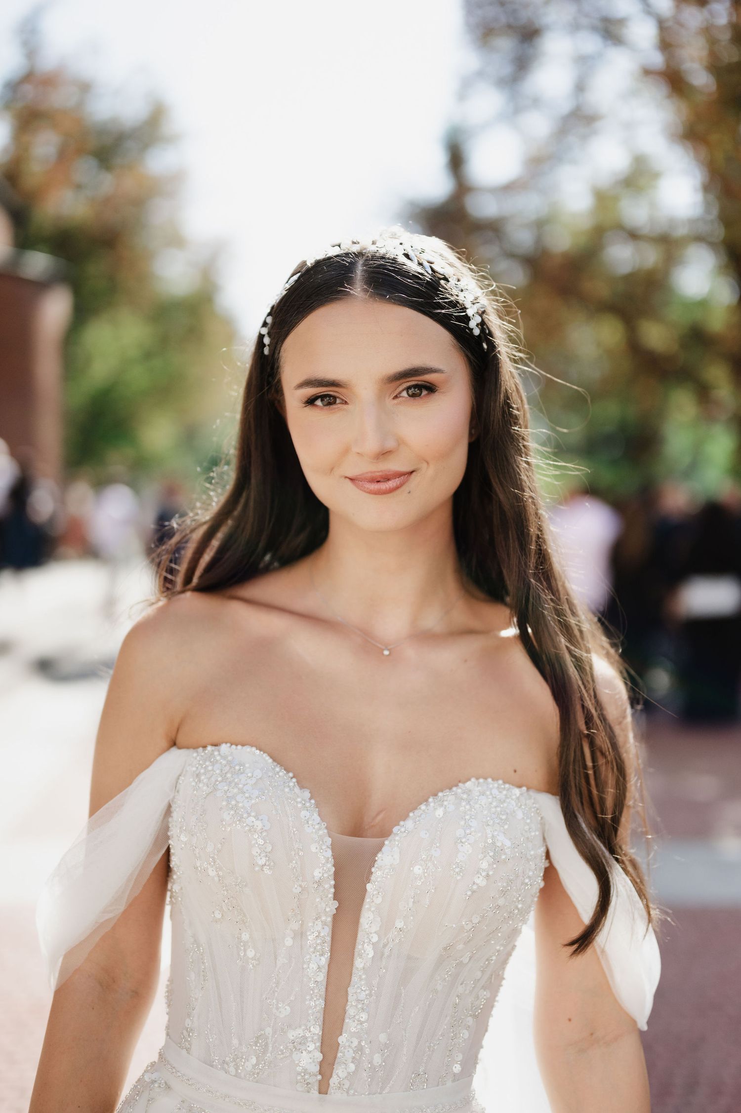 Bride in a detailed white wedding gown with plunging neckline poses outdoors.