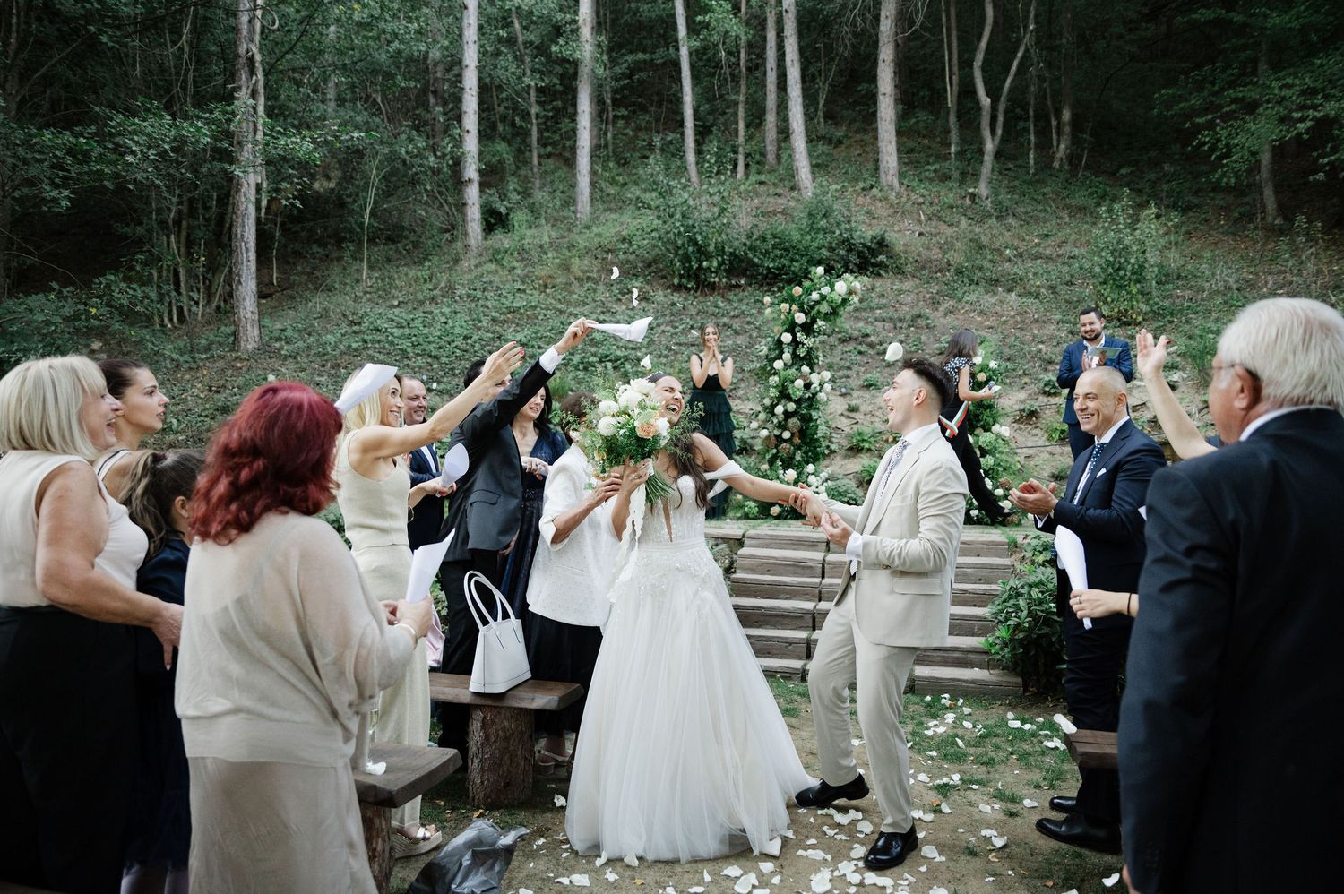 Outdoor wedding ceremony takes place on rustic stone steps surrounded by lush forest scenery.