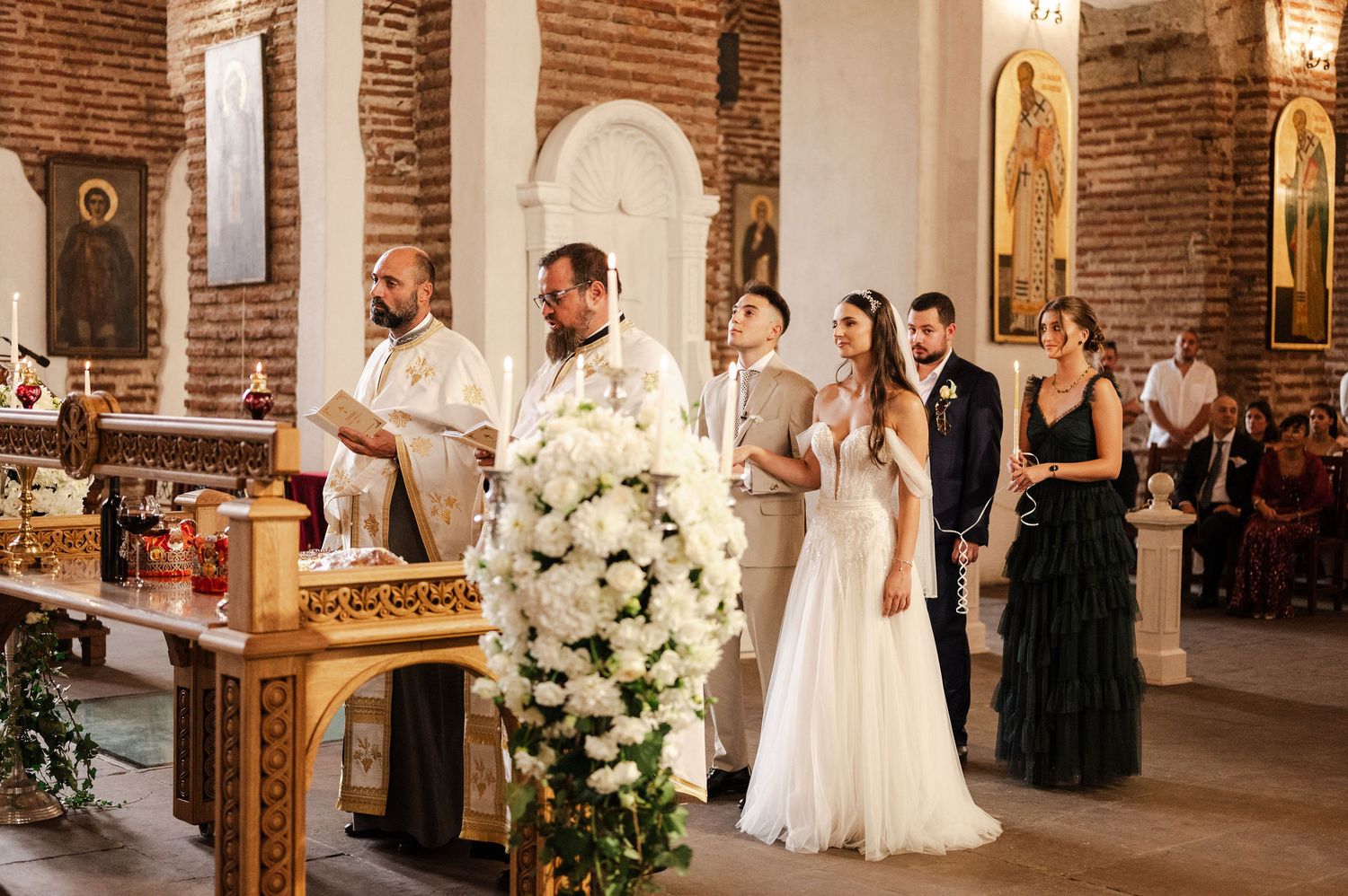 Wedding ceremony in a beautiful brick church with white floral arrangements and candles.