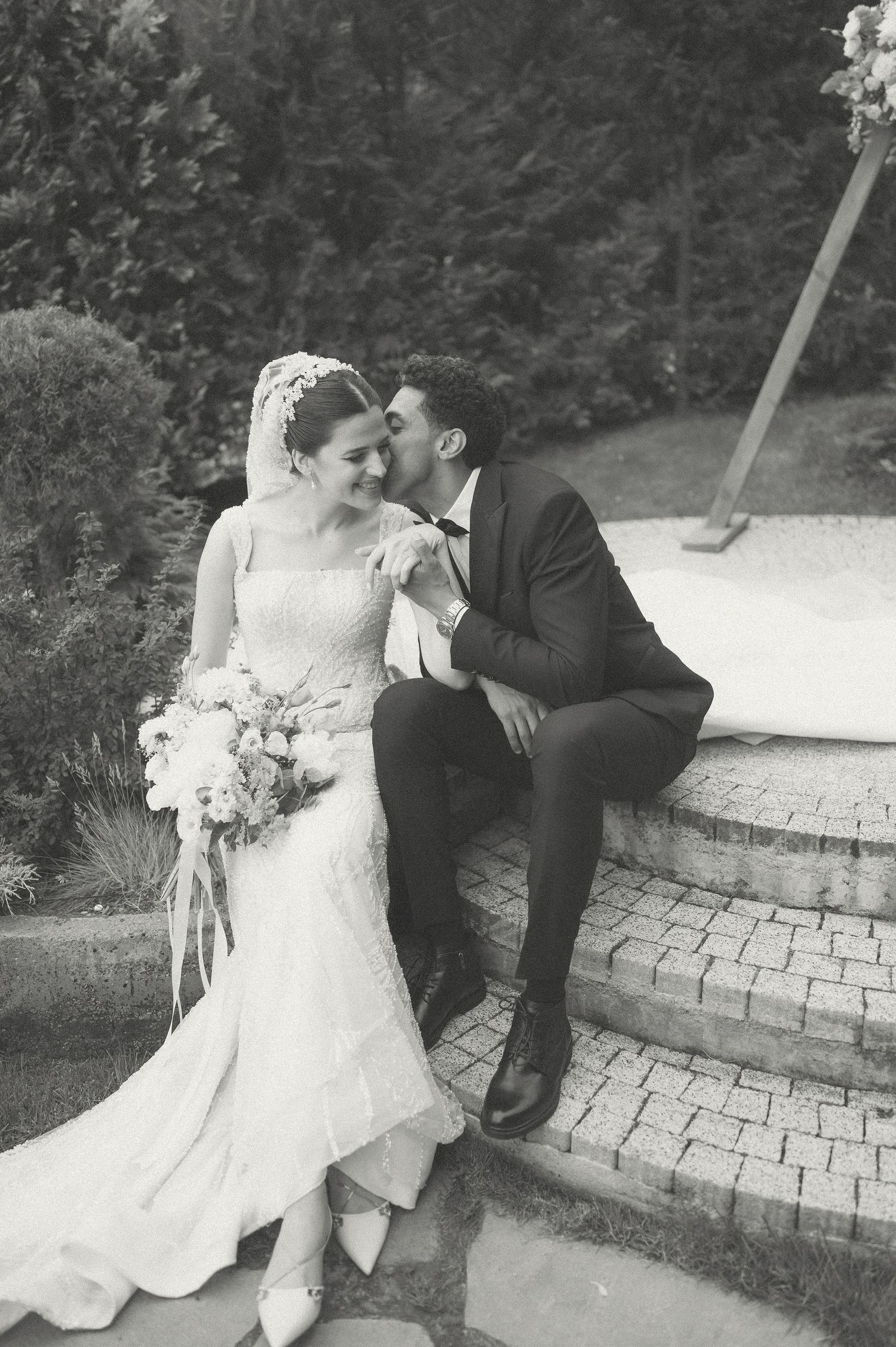 Romantic black and white portraits of newlyweds sitting on stone steps outdoors.