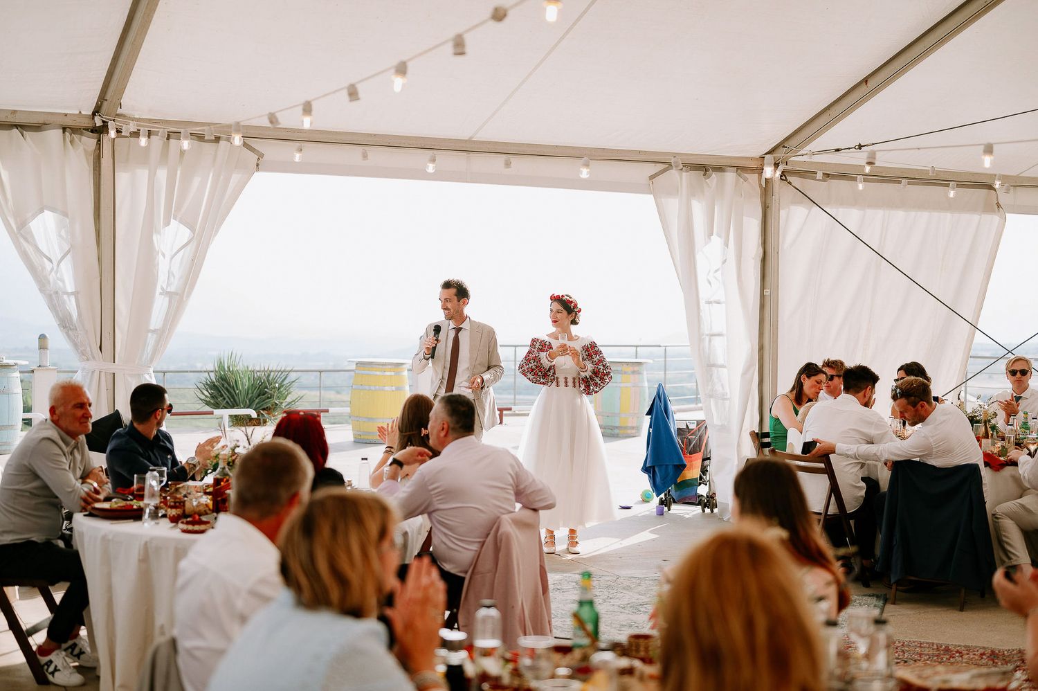 Wedding reception in a white tent with elegant table settings and string lights overhead.