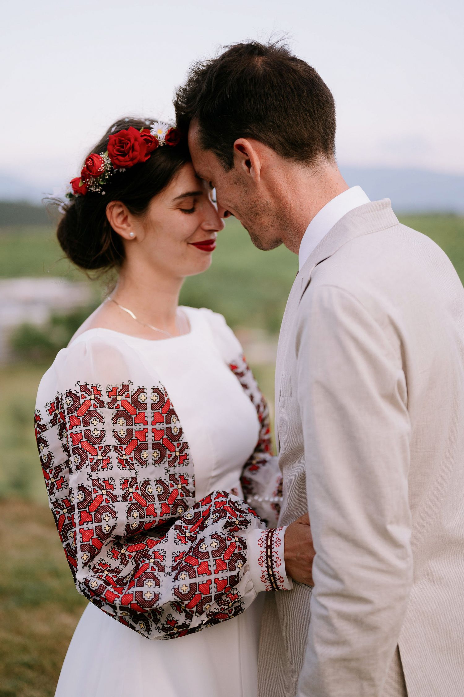 Romantic couple in traditional wedding attire share tender moment on hillside.