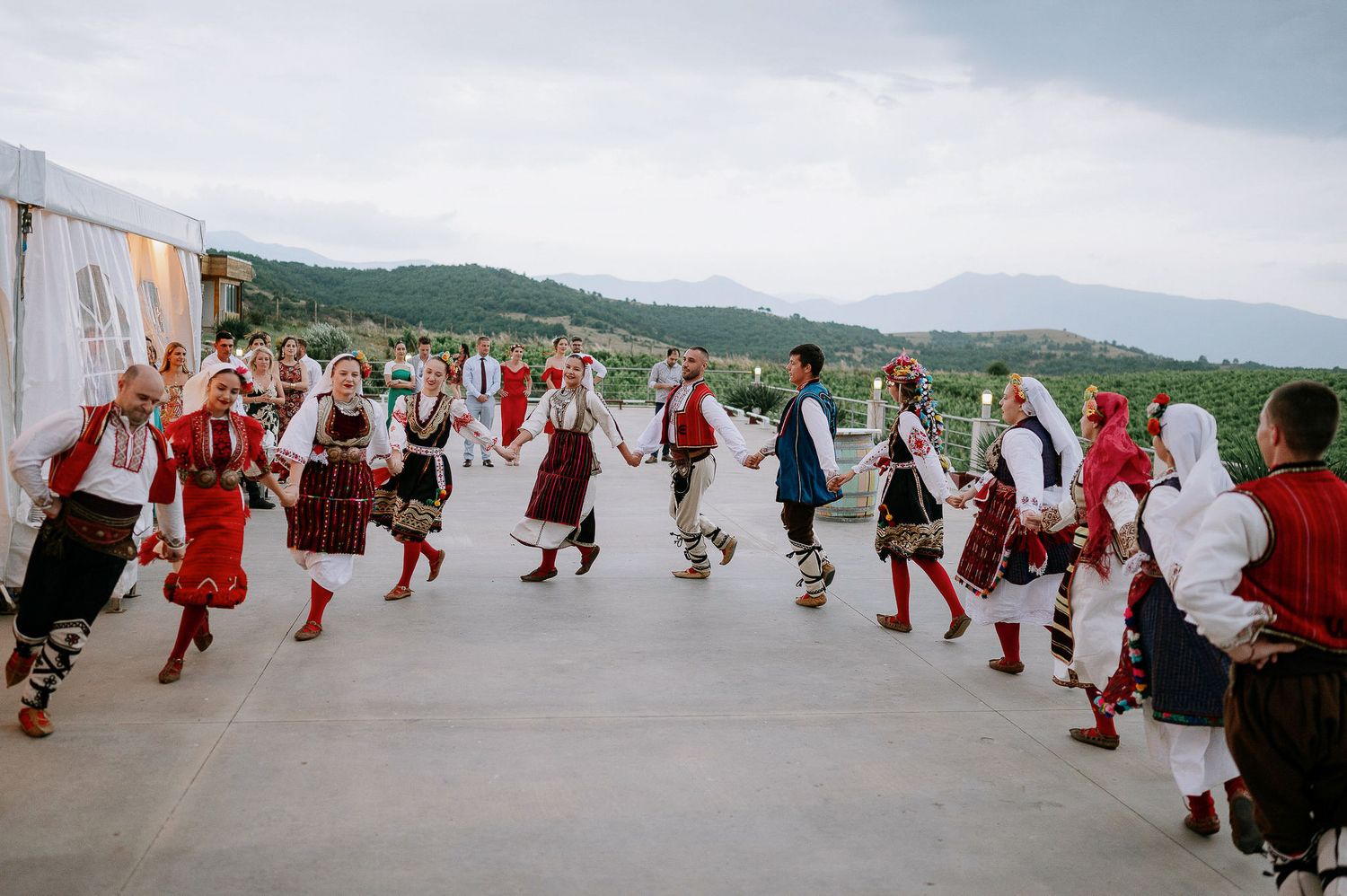 Traditional folk dancers perform in colorful costumes against a mountain backdrop.