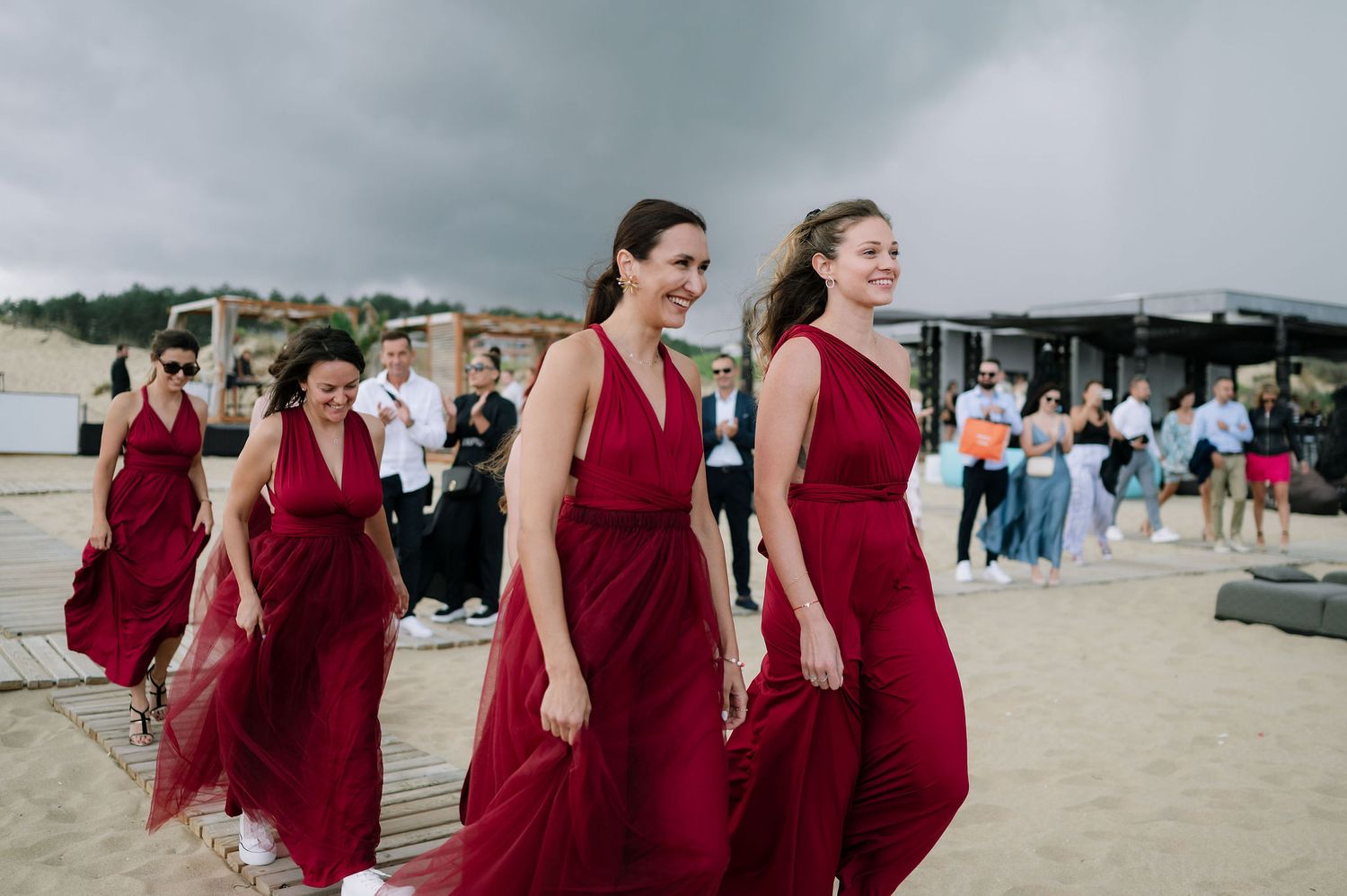 Bridesmaids in burgundy dresses walking together on beach during wedding.