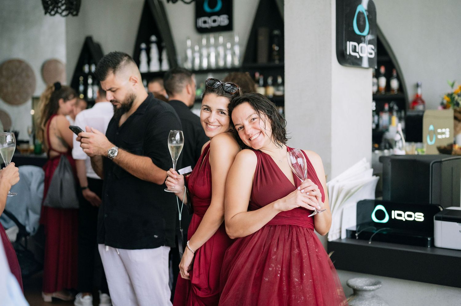 Guests in burgundy dresses and casual attire mingle at an elegant bar during a celebration event.