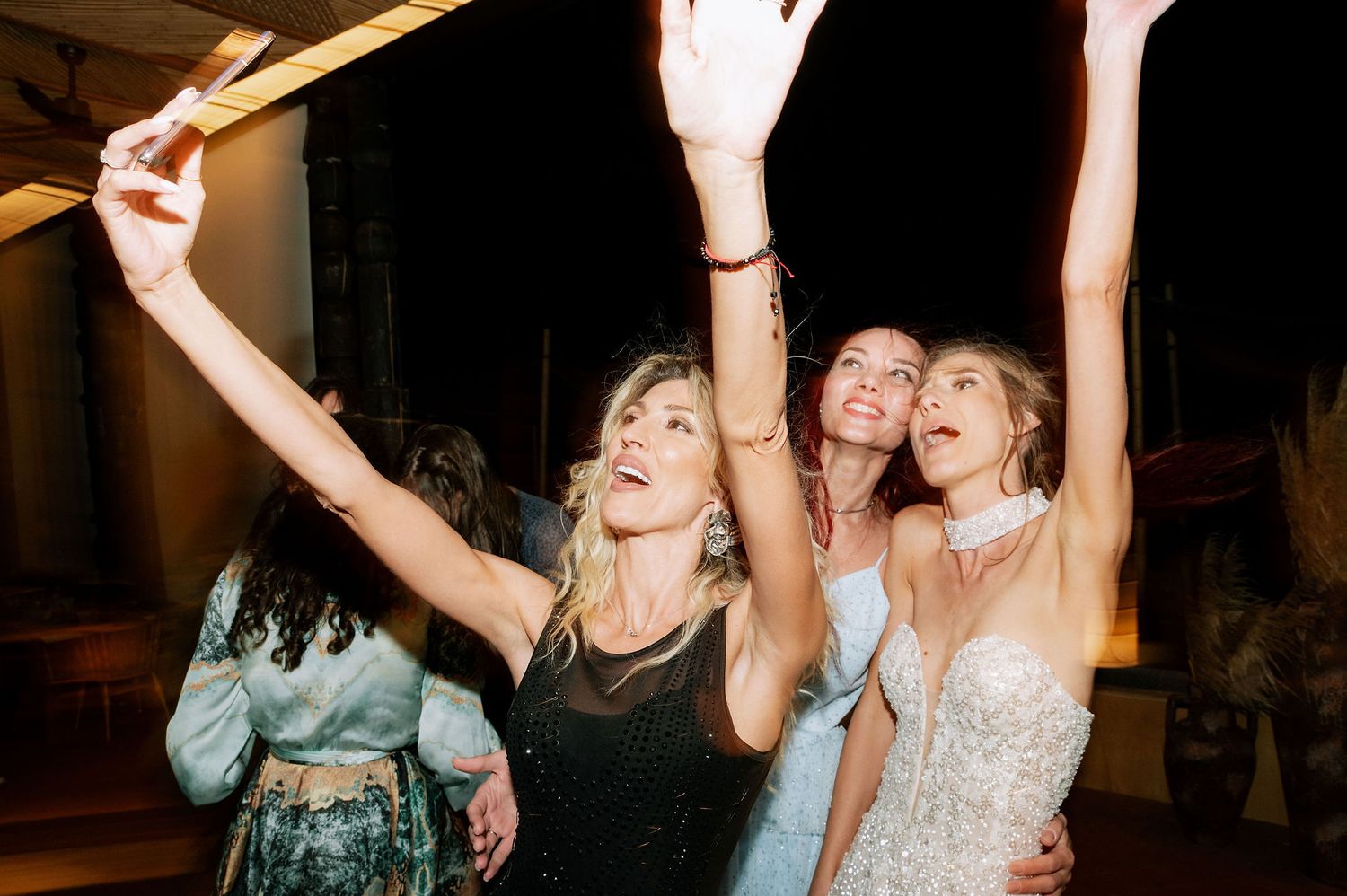 Partygoers with raised arms dancing together under warm indoor lighting.