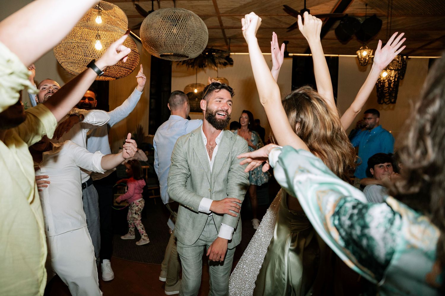 Energetic crowd dancing and celebrating at a dimly lit indoor party venue with hands raised in excitement.