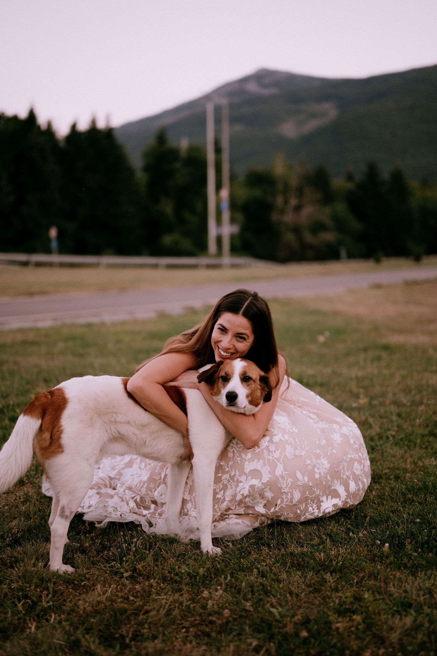 Sweet moment with brown and white dog and wedding dress in mountain setting.