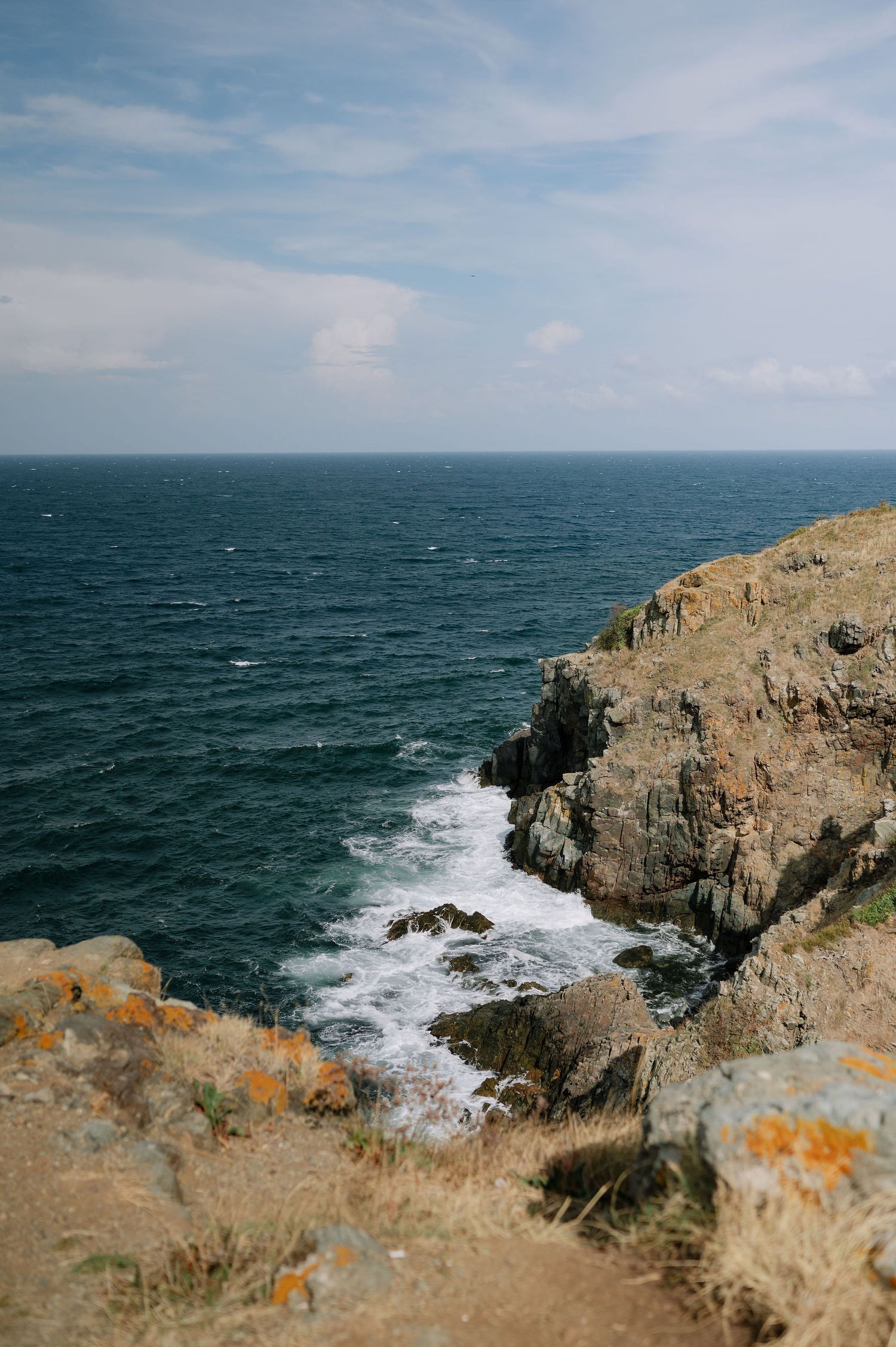 Dramatic coastal cliffs with crashing waves against rocky shores under a blue sky.