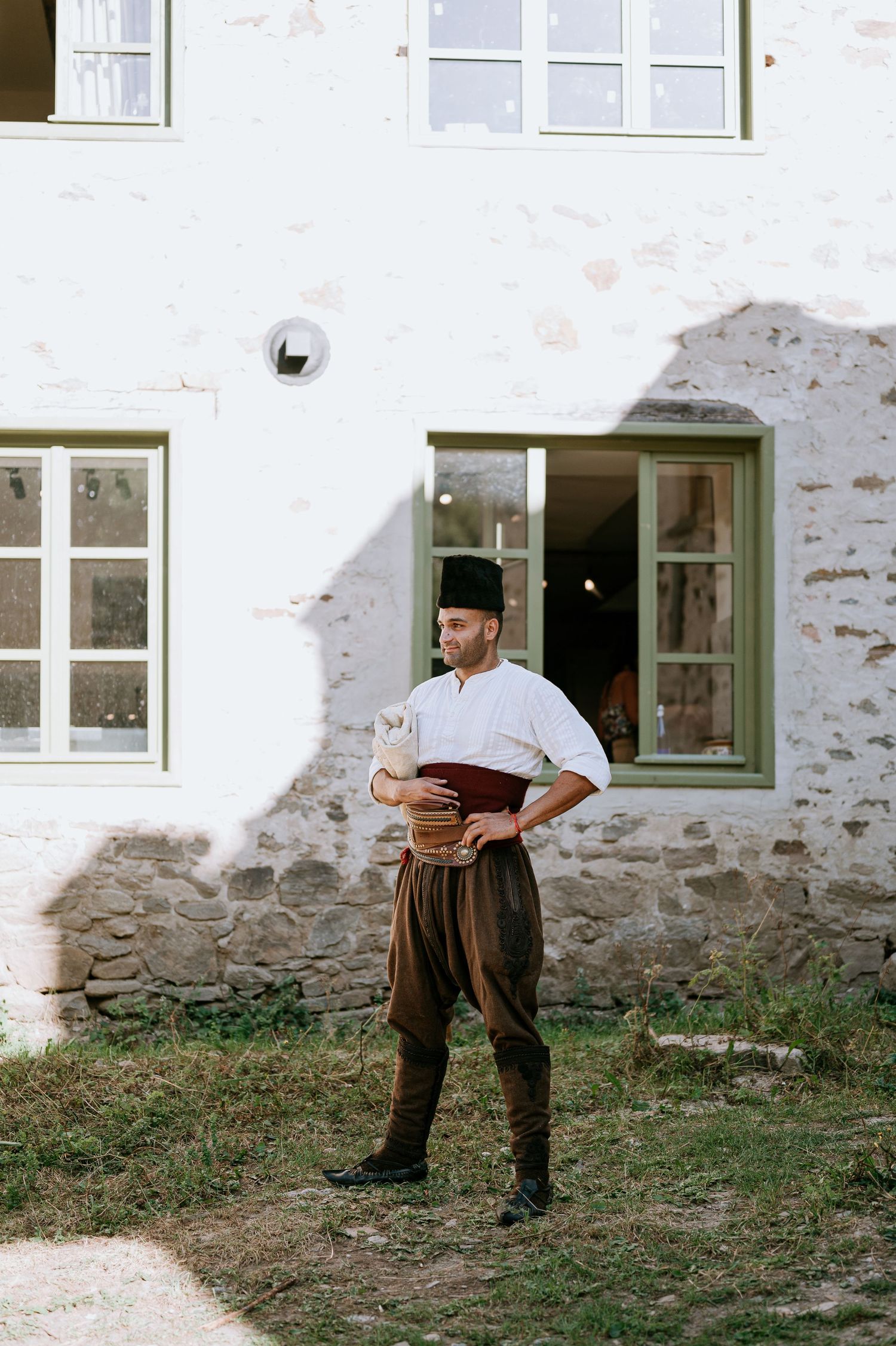 Traditional folk costume worn against white building exterior with green window frames.