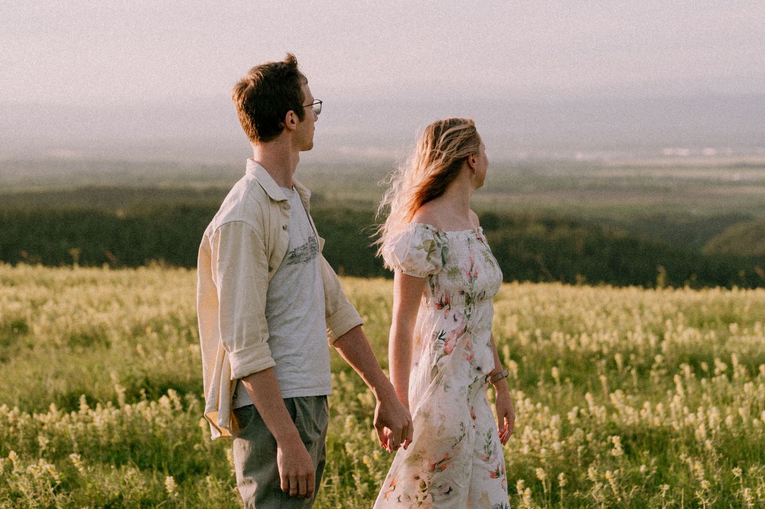 A couple shares a tender moment in a sunlit meadow with rolling hills in the background.