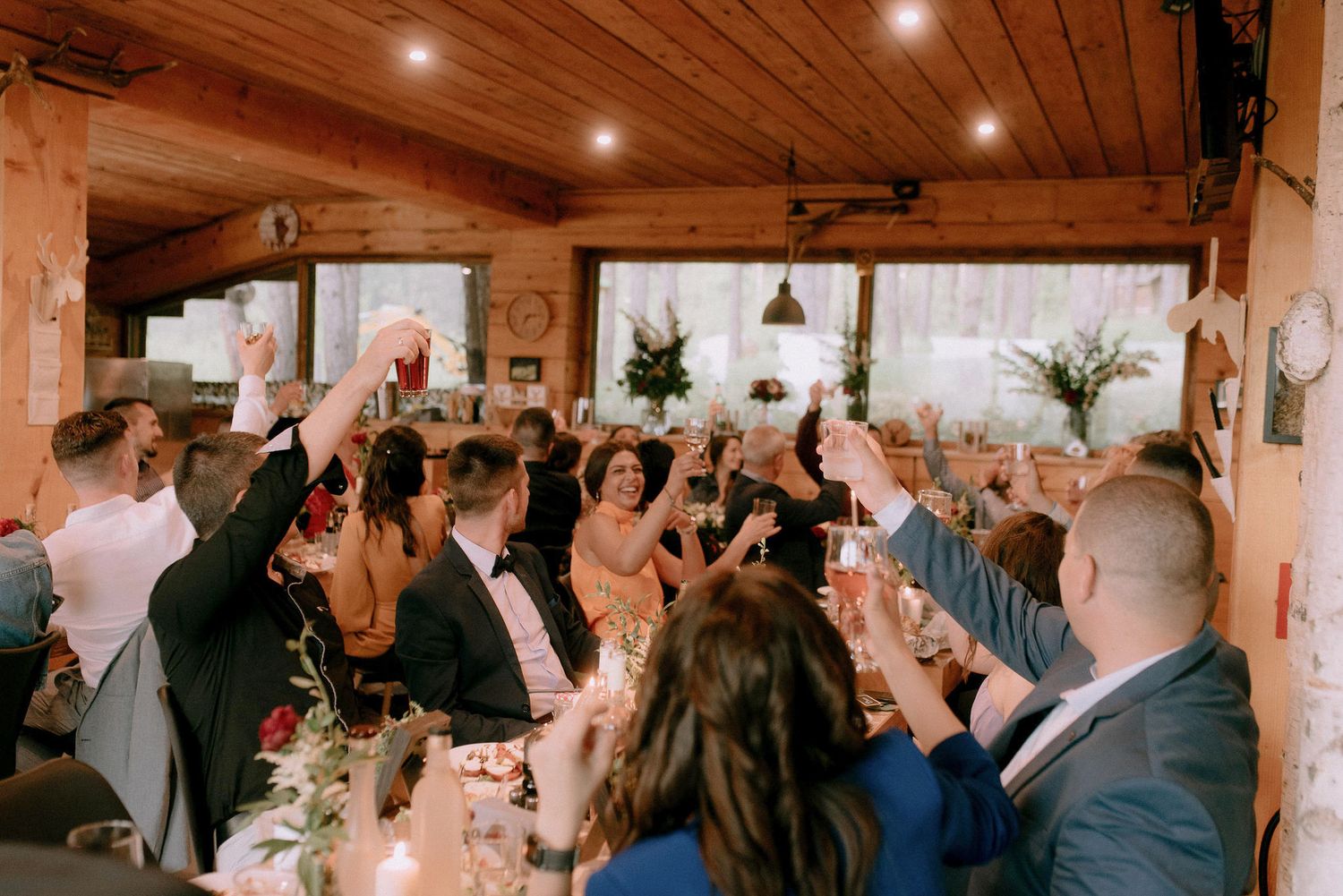 Wedding reception guests raising glasses for a toast inside rustic wooden venue.