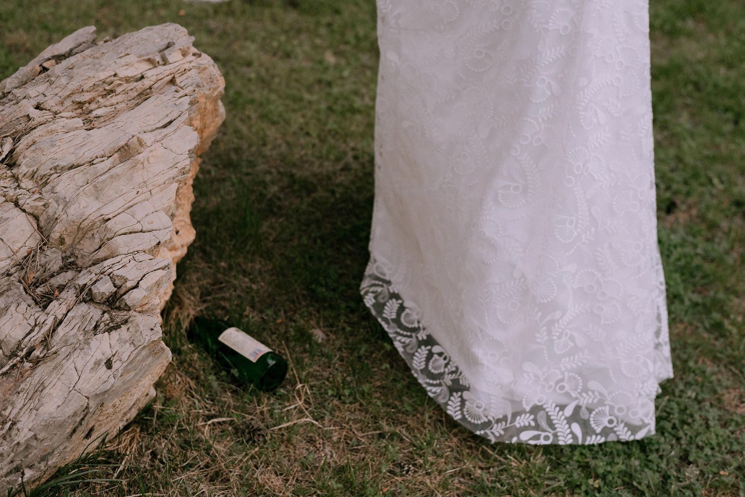 Close-up detail of a white lace wedding dress hem against grass.