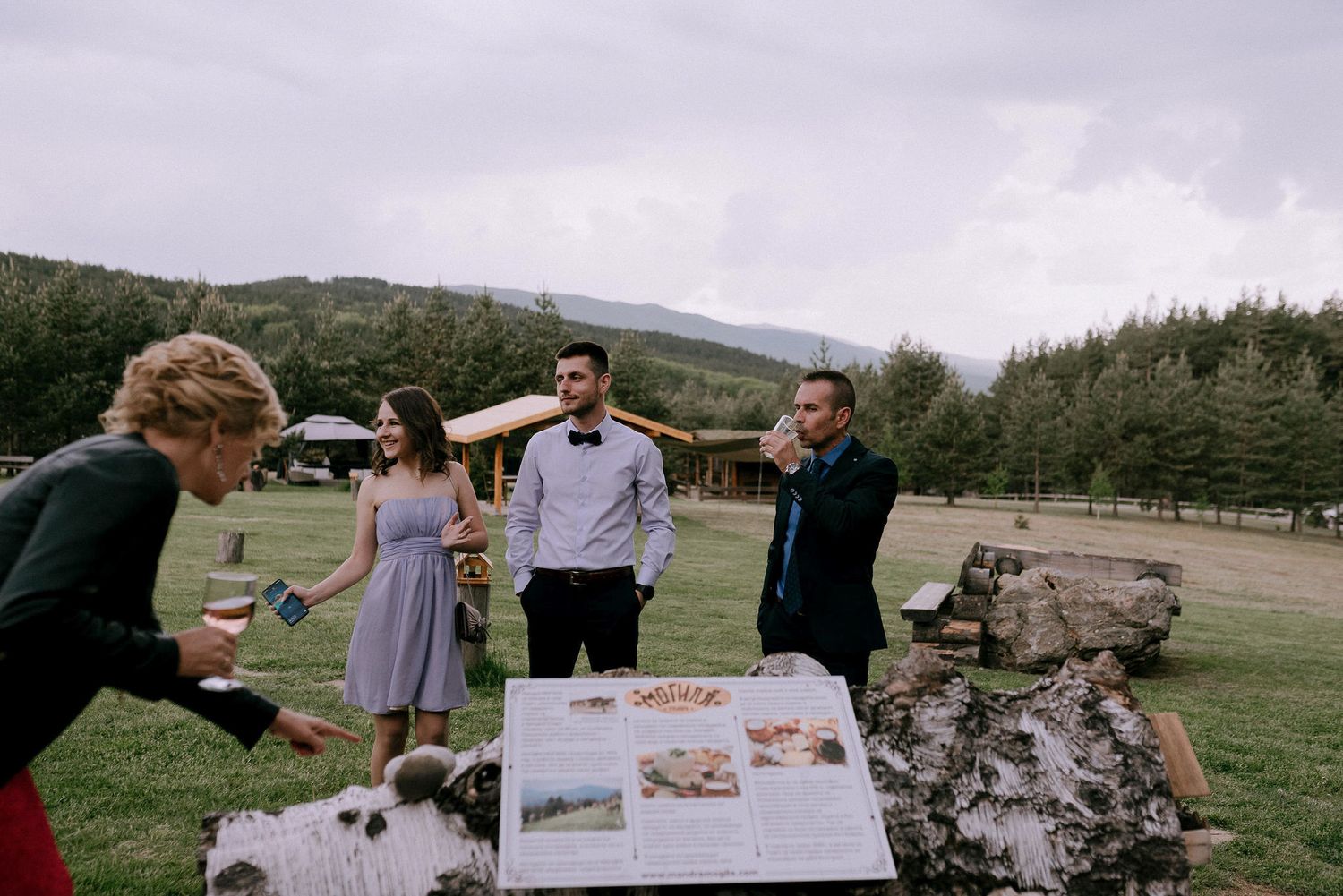 Wedding guests viewing photos near stone wall at outdoor mountain venue.