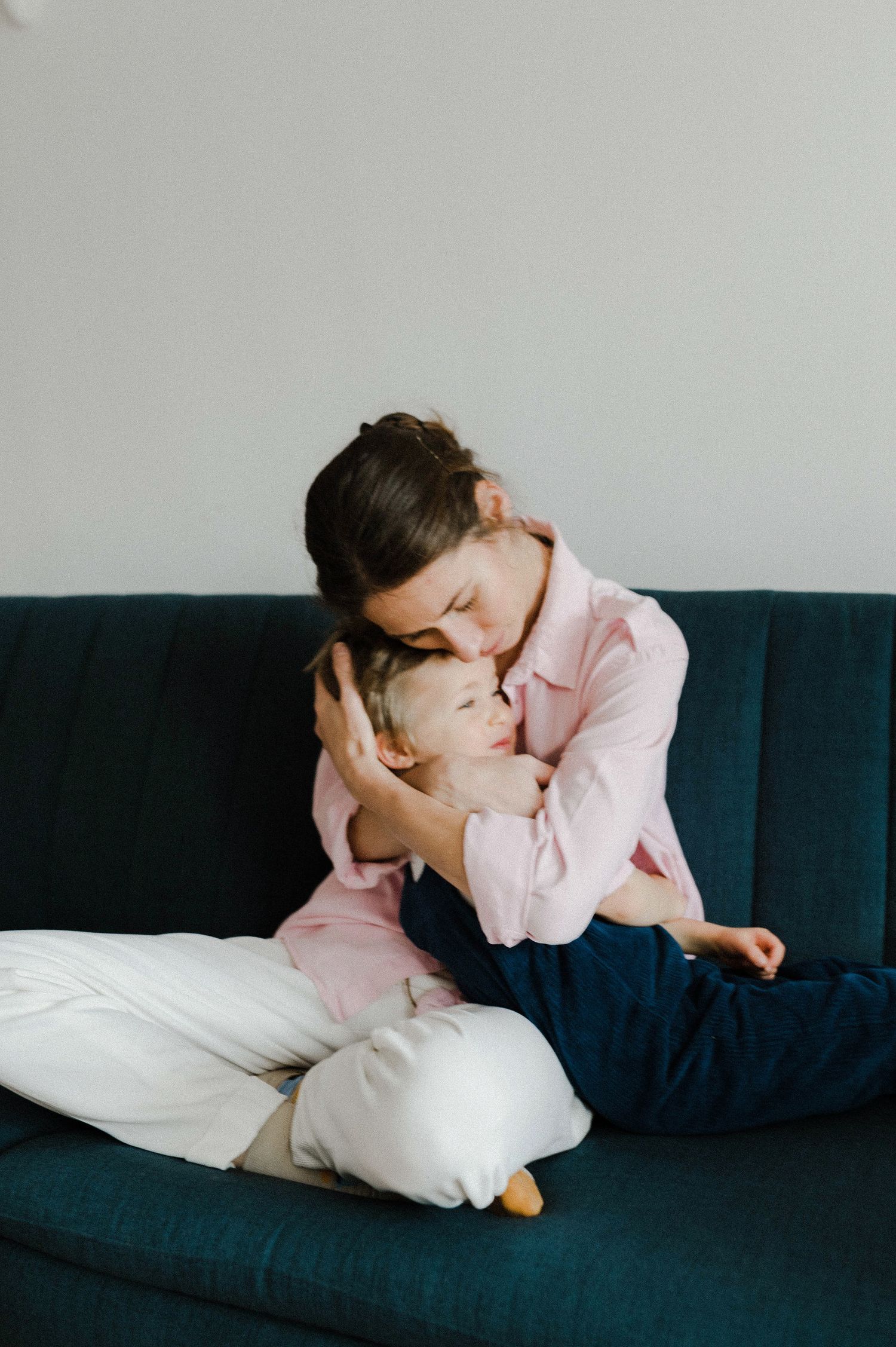 A child in a pink sweater and white pants rests sleepily on a navy blue couch.