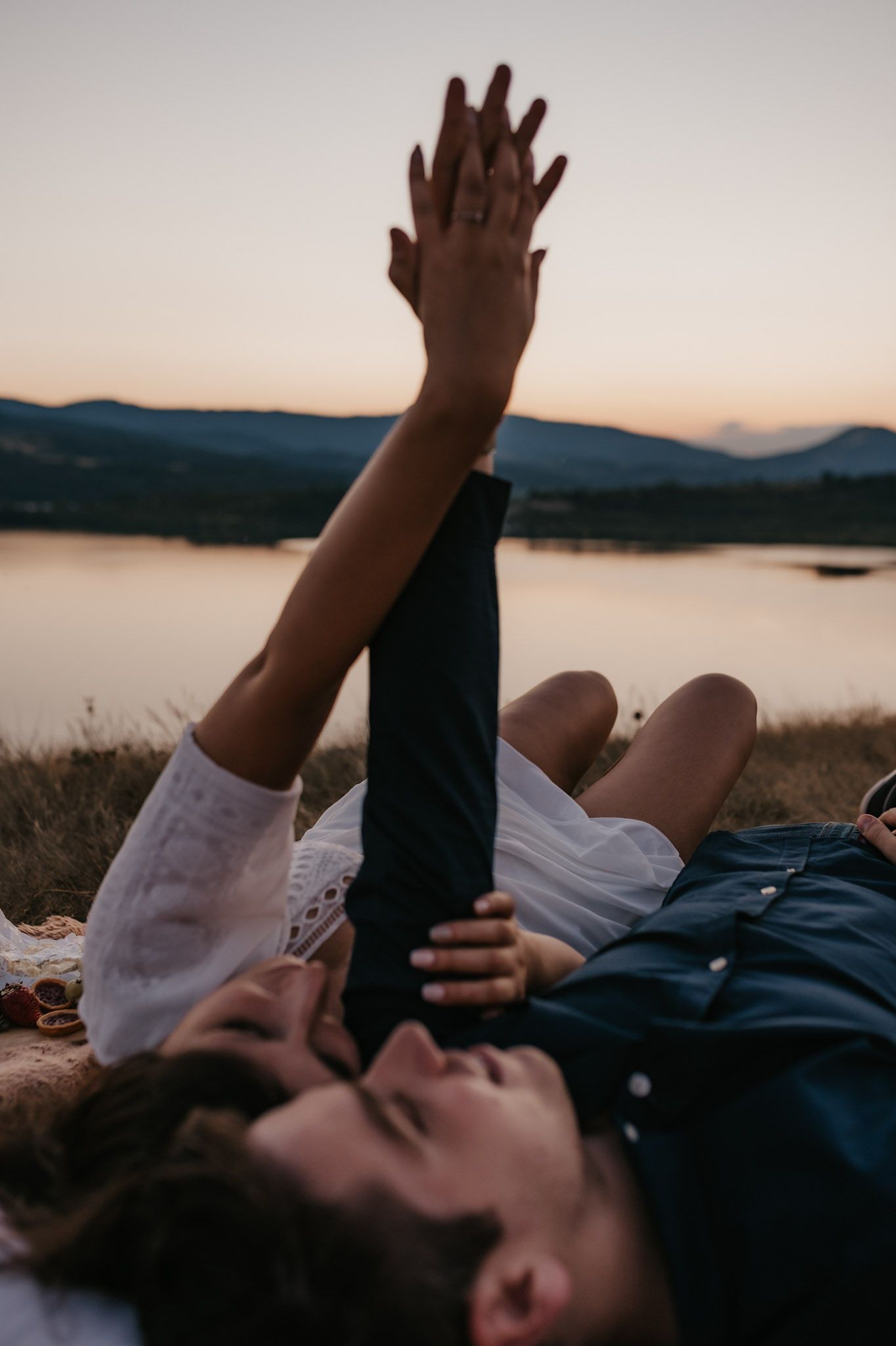 Person lying down with raised hand against sunset mountain backdrop.