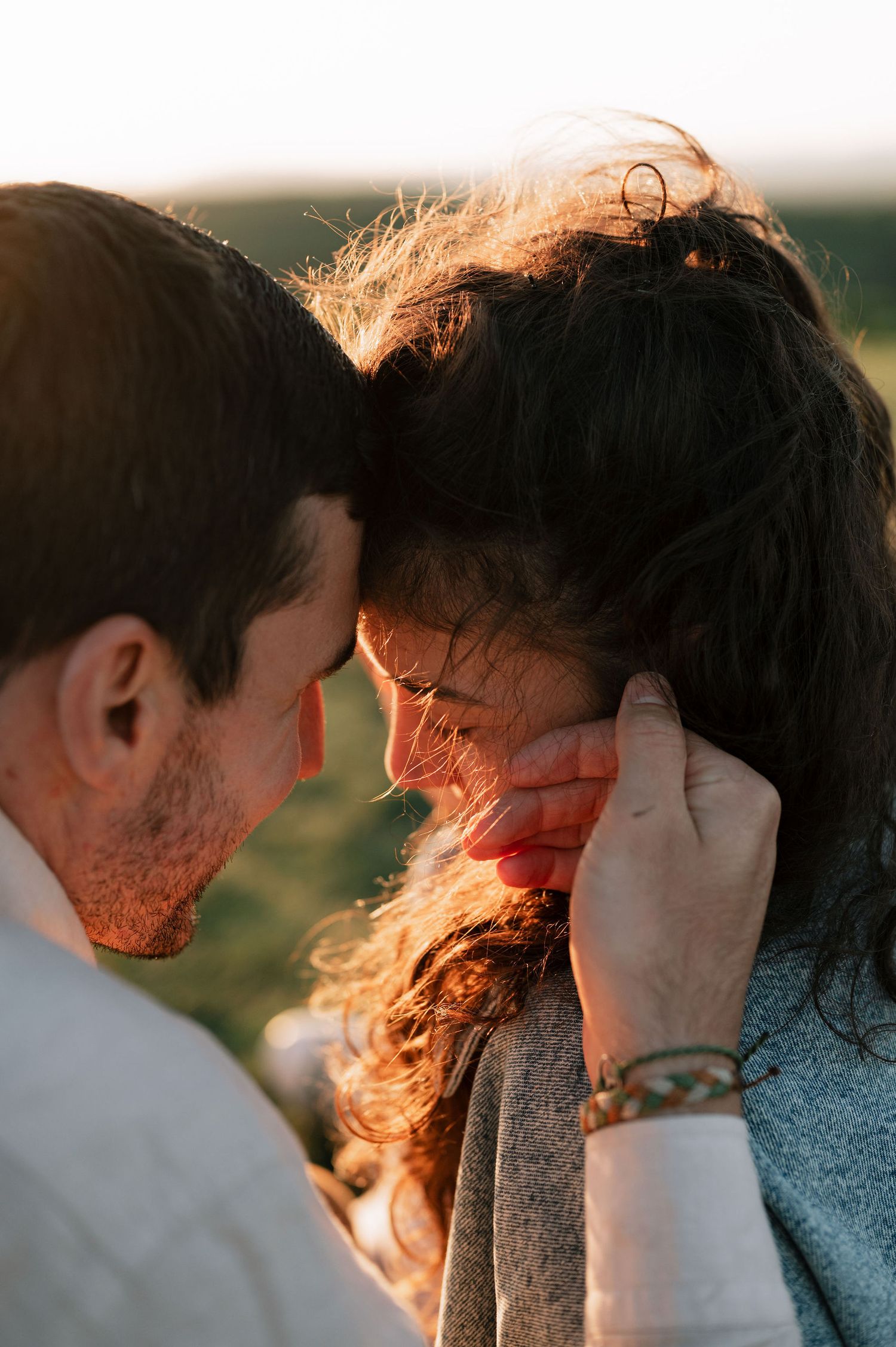 A romantic couple embraces in golden sunlight as wind blows through their hair during sunset.