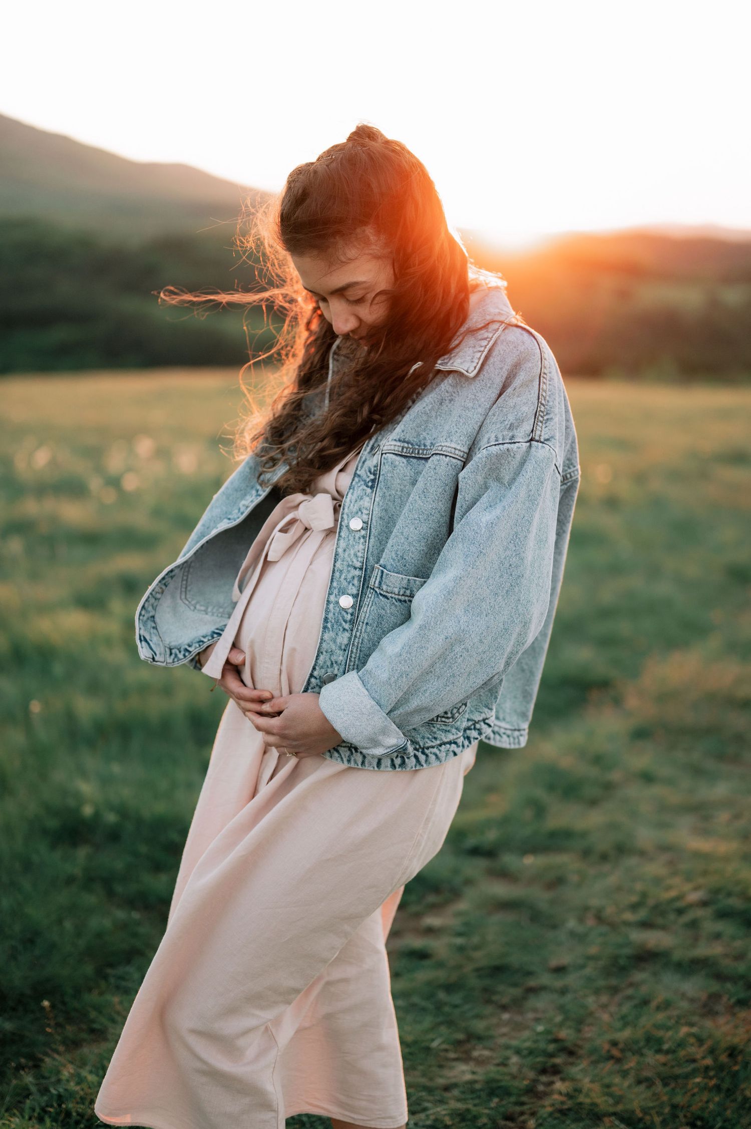 A dreamy sunset portrait of someone in a denim jacket and light dress twirling in a grassy meadow.