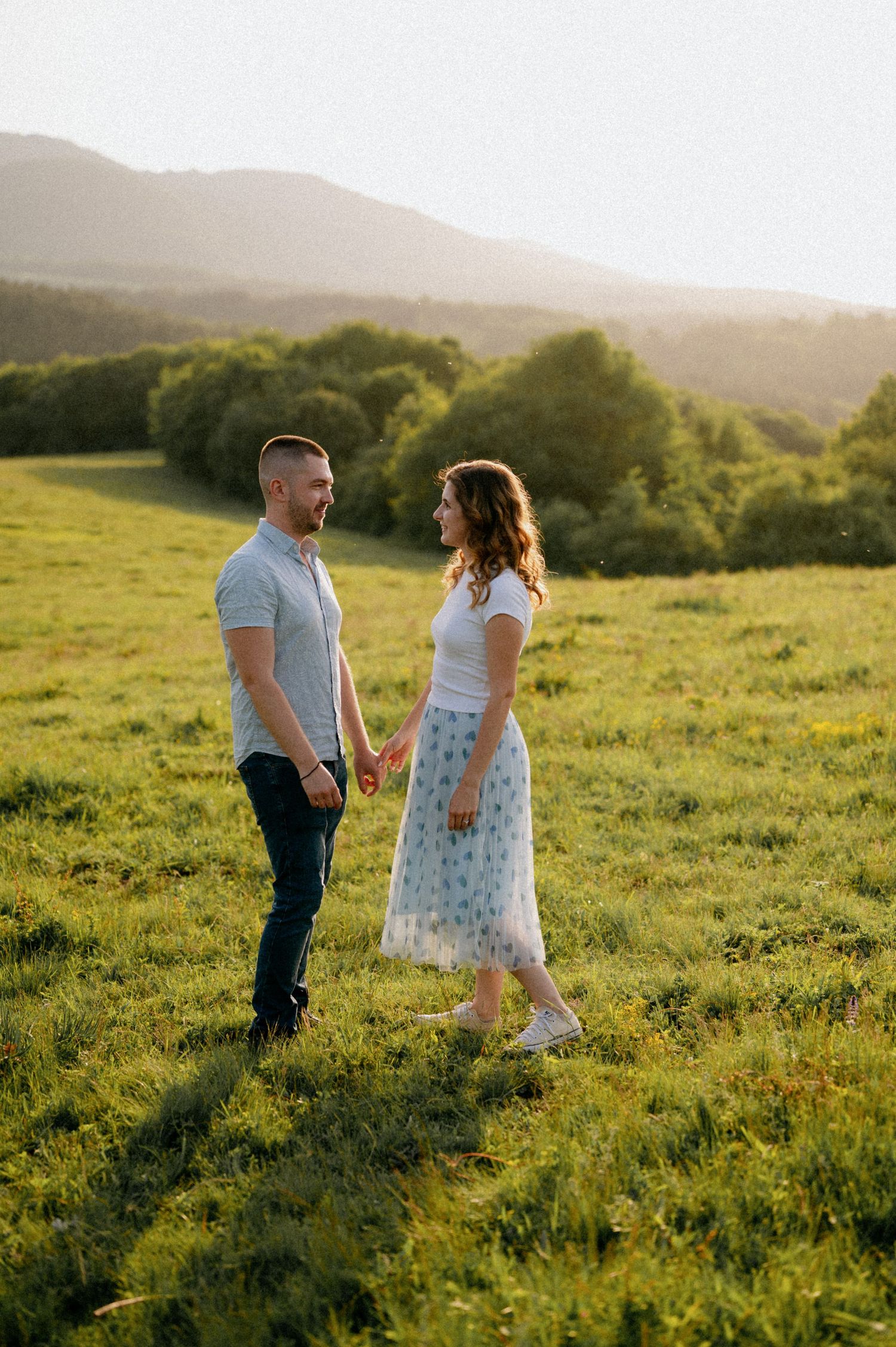 A couple dances together in a green meadow bathed in warm evening sunlight.