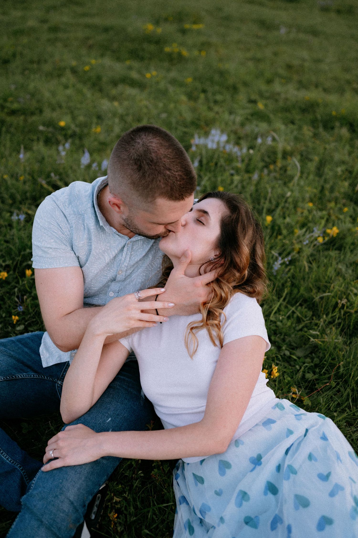 Tender moment between couple lying in grass with scattered yellow wildflowers.