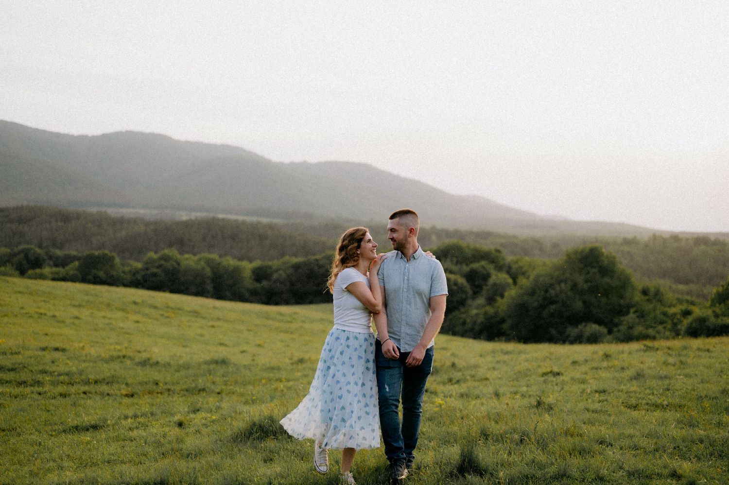 Couple walking hand in hand through a mountainside field at sunset.