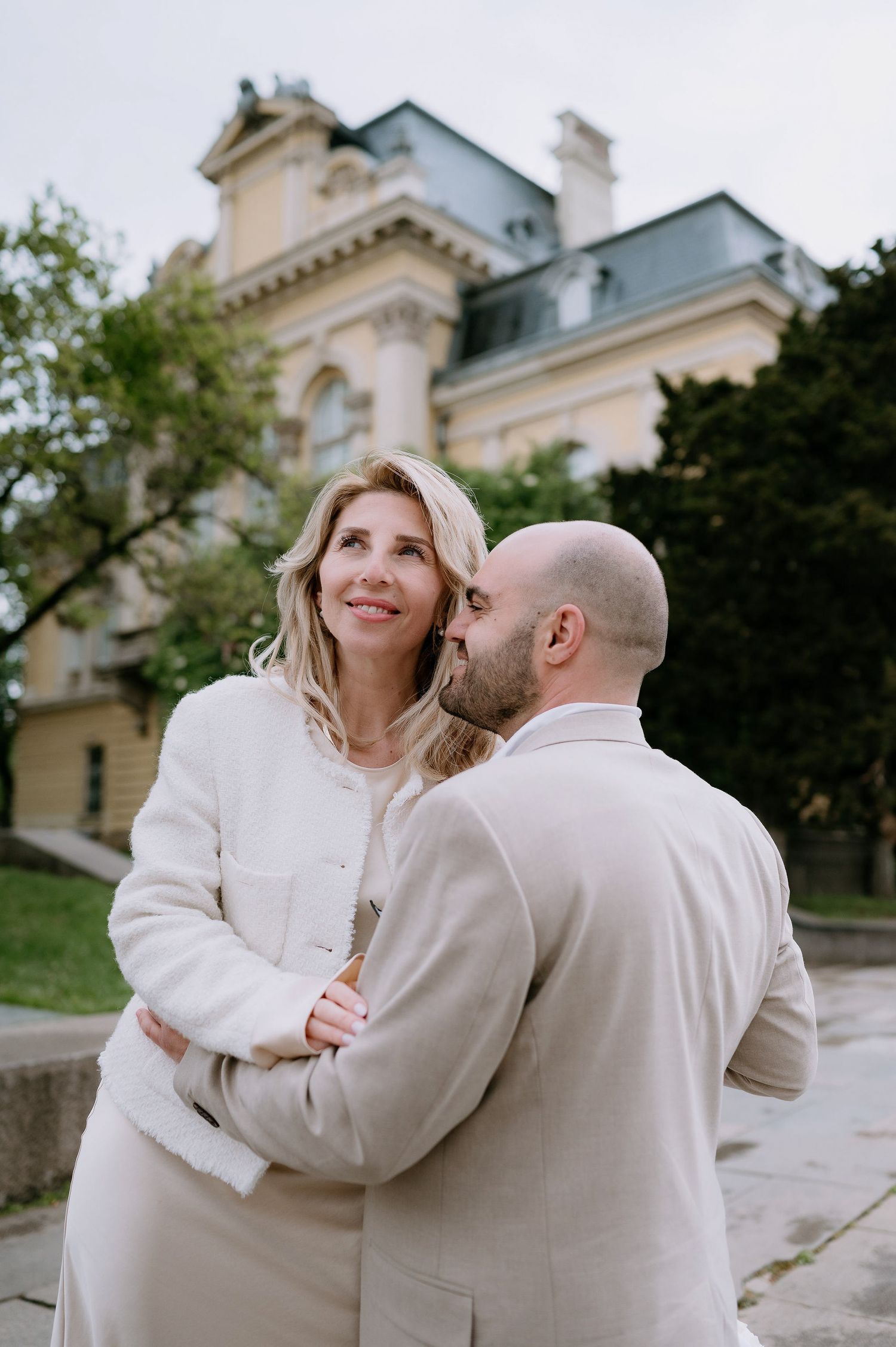 A couple dressed in white shares an intimate moment outside a classical architectural setting.