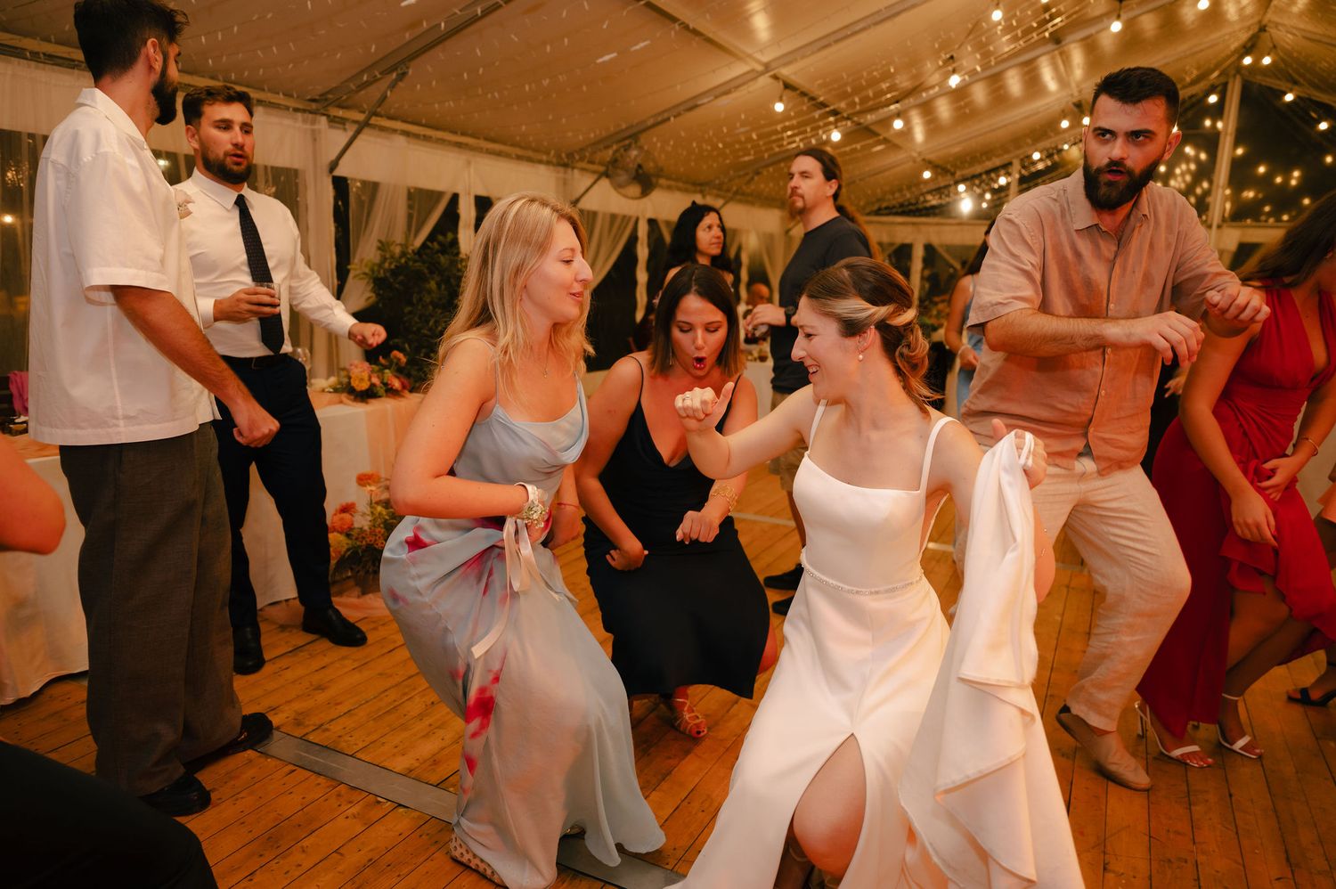 Wedding guests dance and celebrate on a warmly lit dance floor during a reception party.