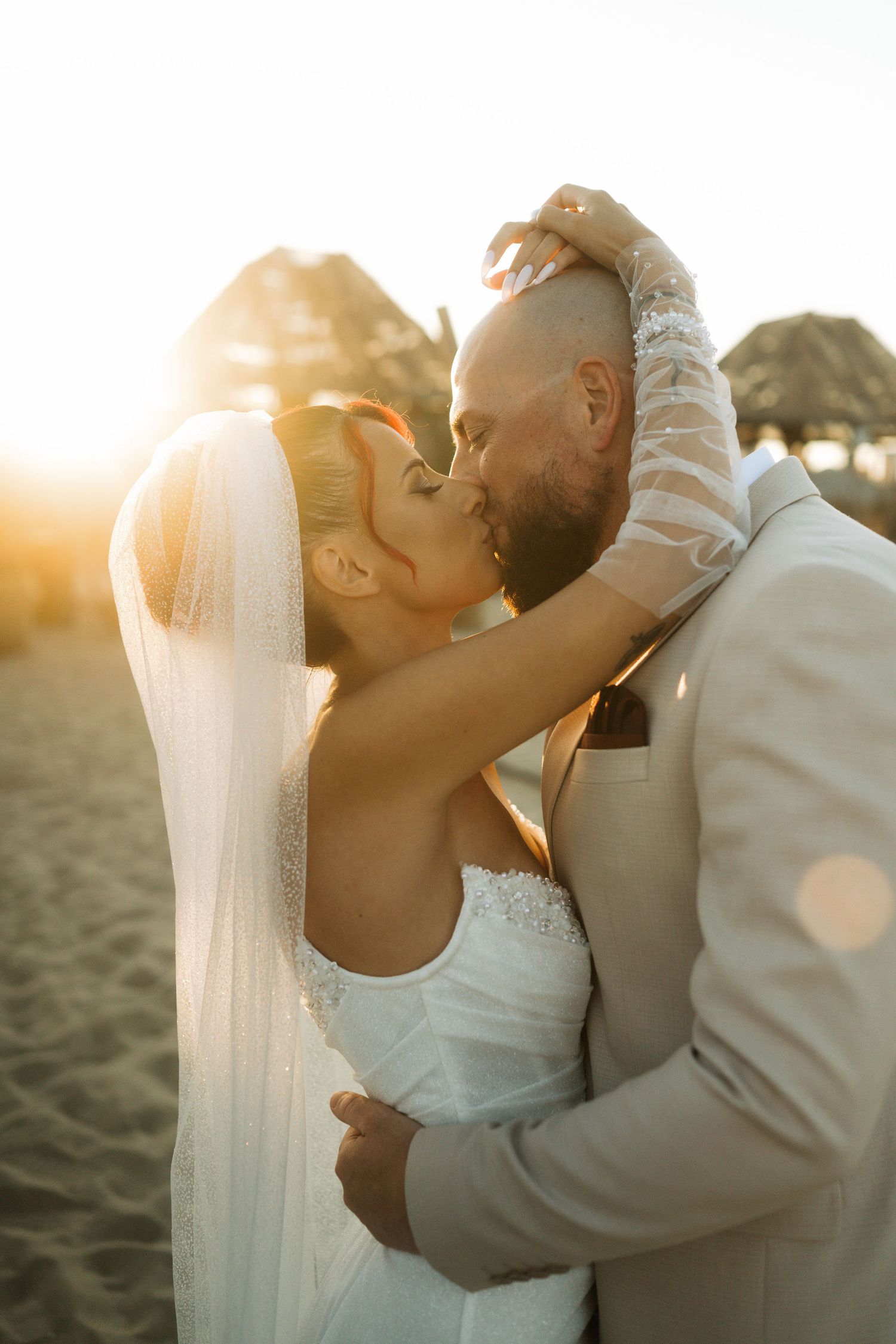 Romantic beach wedding couple sharing intimate moments at sunset with flowing white veil and golden light.