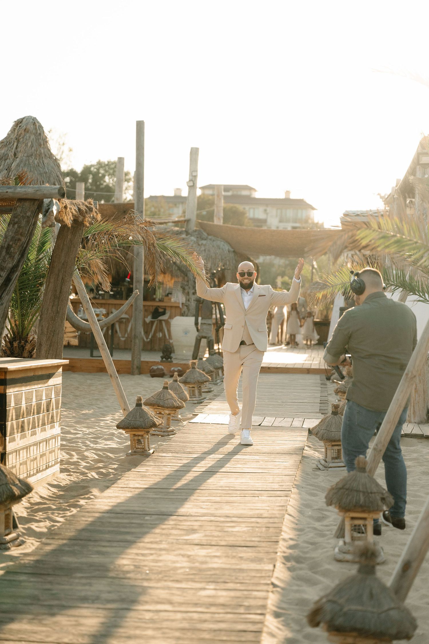 Couple sits on wooden deck chairs at sunset overlooking a beachfront scene in warm golden light.
