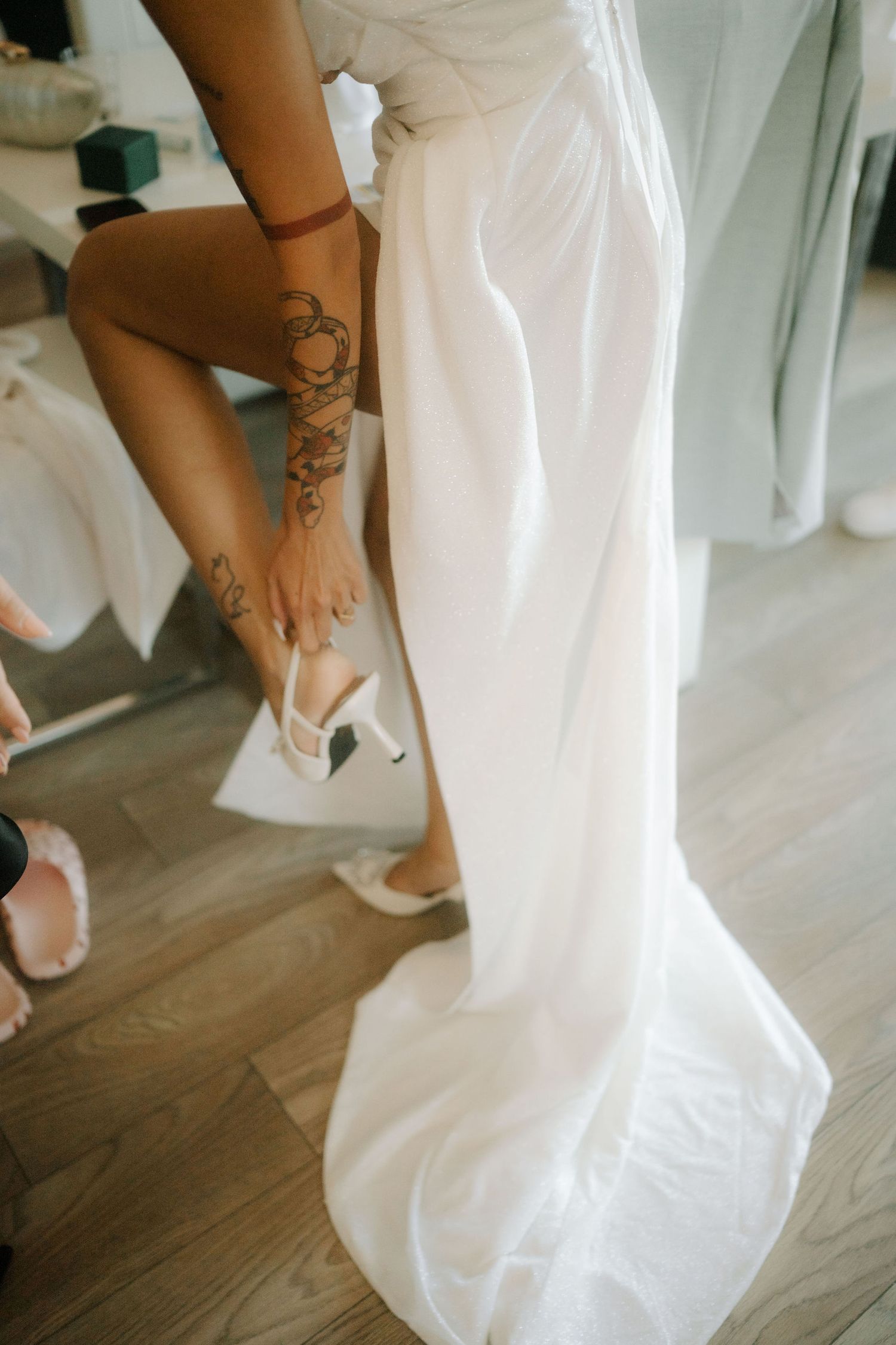 Close-up views of feet with henna tattoos wearing white flip flops under flowing white fabric on wooden floor.