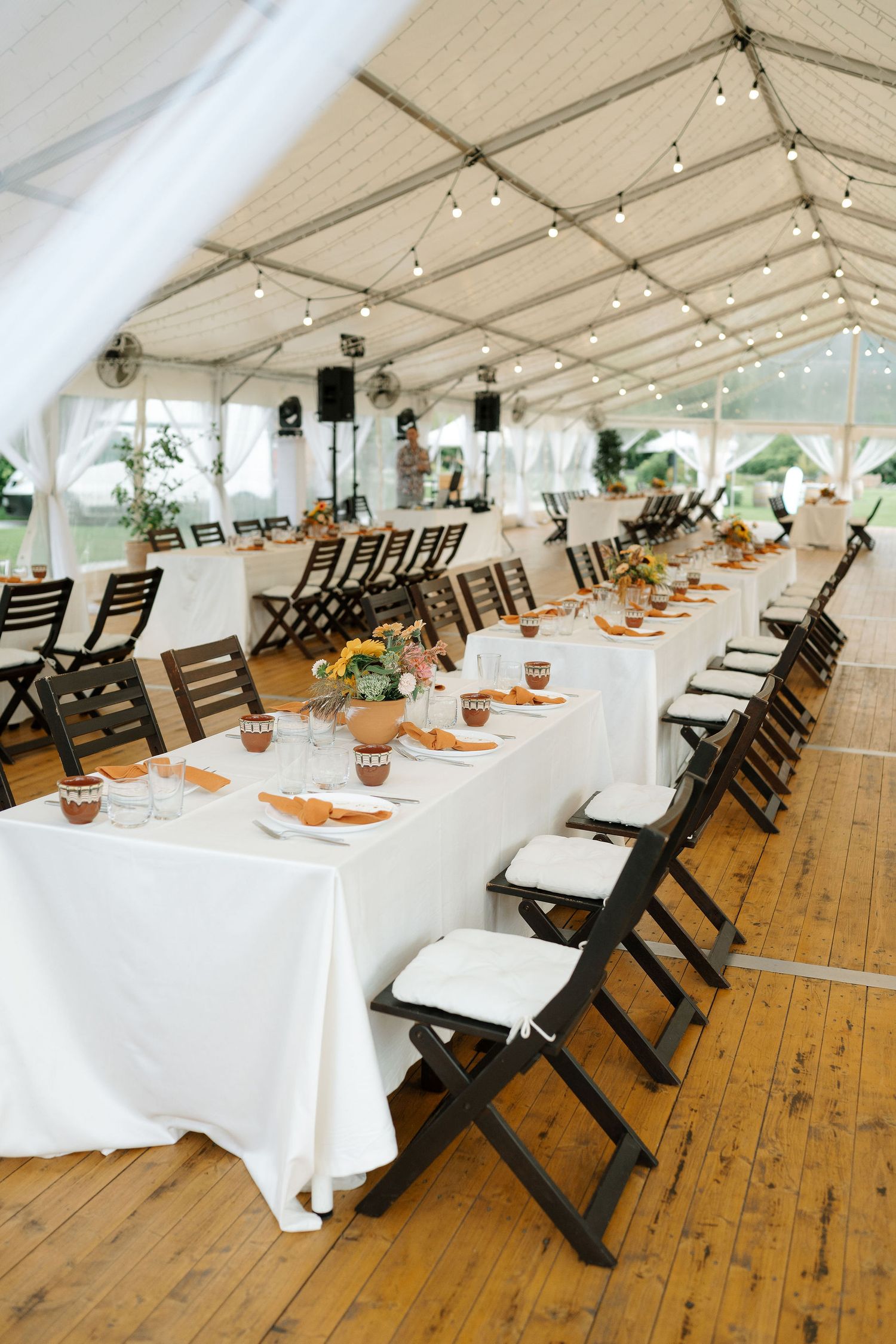 Wedding reception tent interior with wooden floors, white tablecloths, and string lights creating an elegant dining setup.