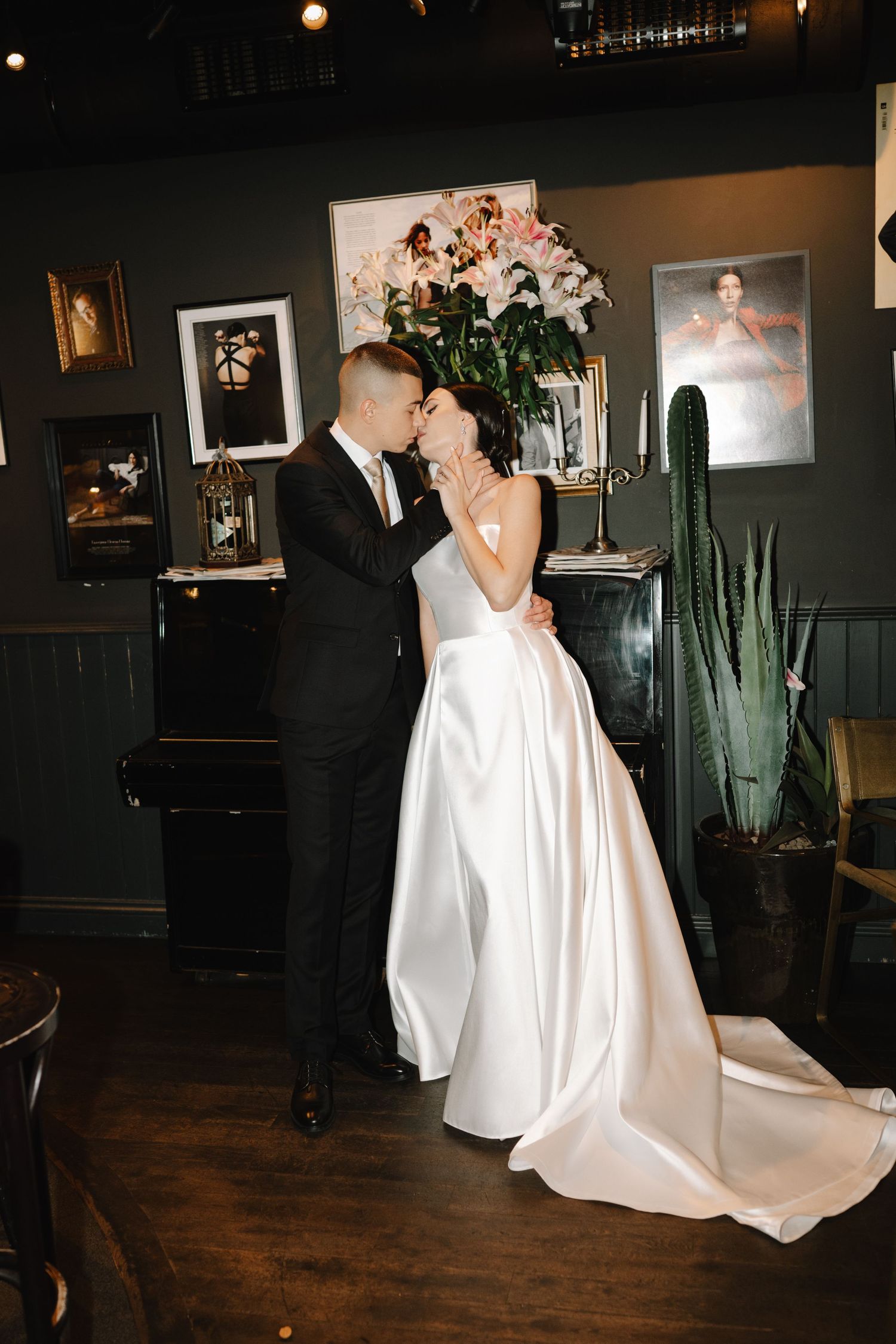 Newlyweds dance and embrace in a dimly lit venue with dark walls and hardwood floors.