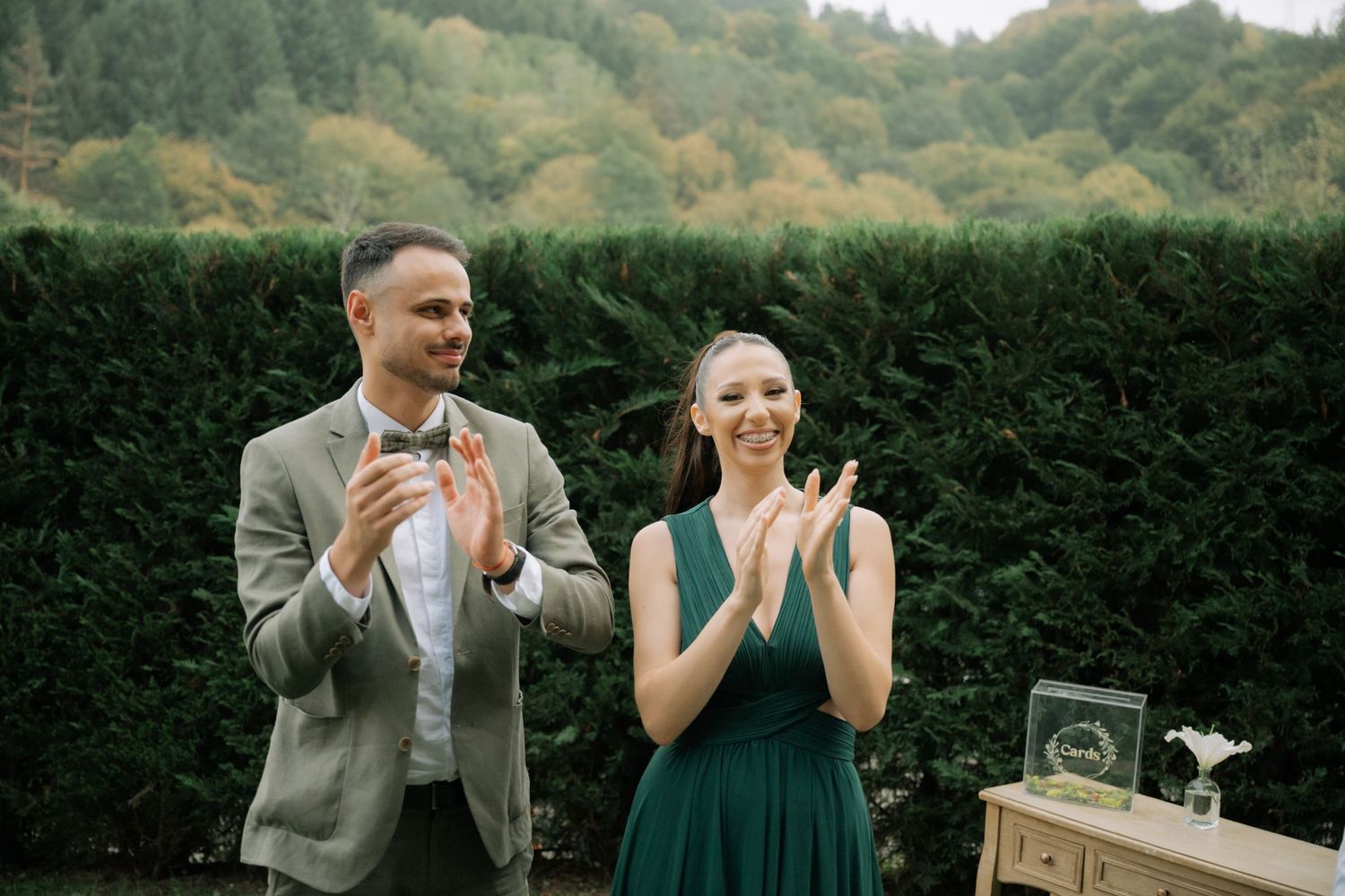 A couple celebrates during an outdoor garden wedding ceremony surrounded by lush green hedges and trees.