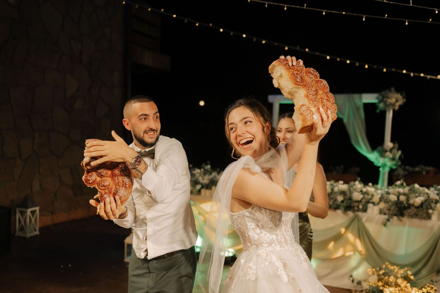 Newlywed couple shares joyful dance moves together at their evening wedding reception with decorative lighting.