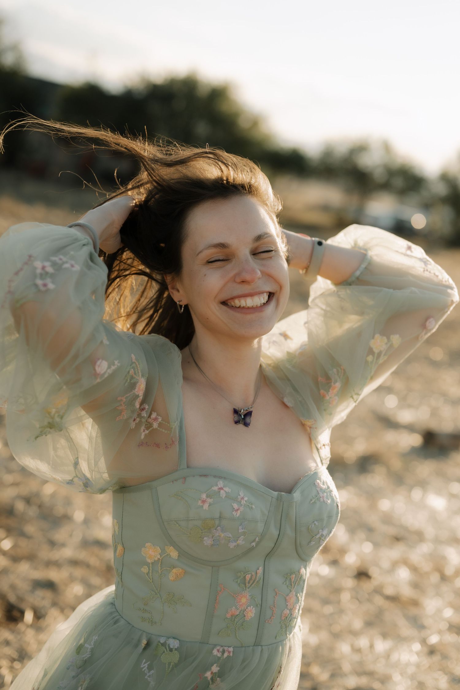 A person in a mint green floral dress poses joyfully in golden sunlight during a summer photoshoot.