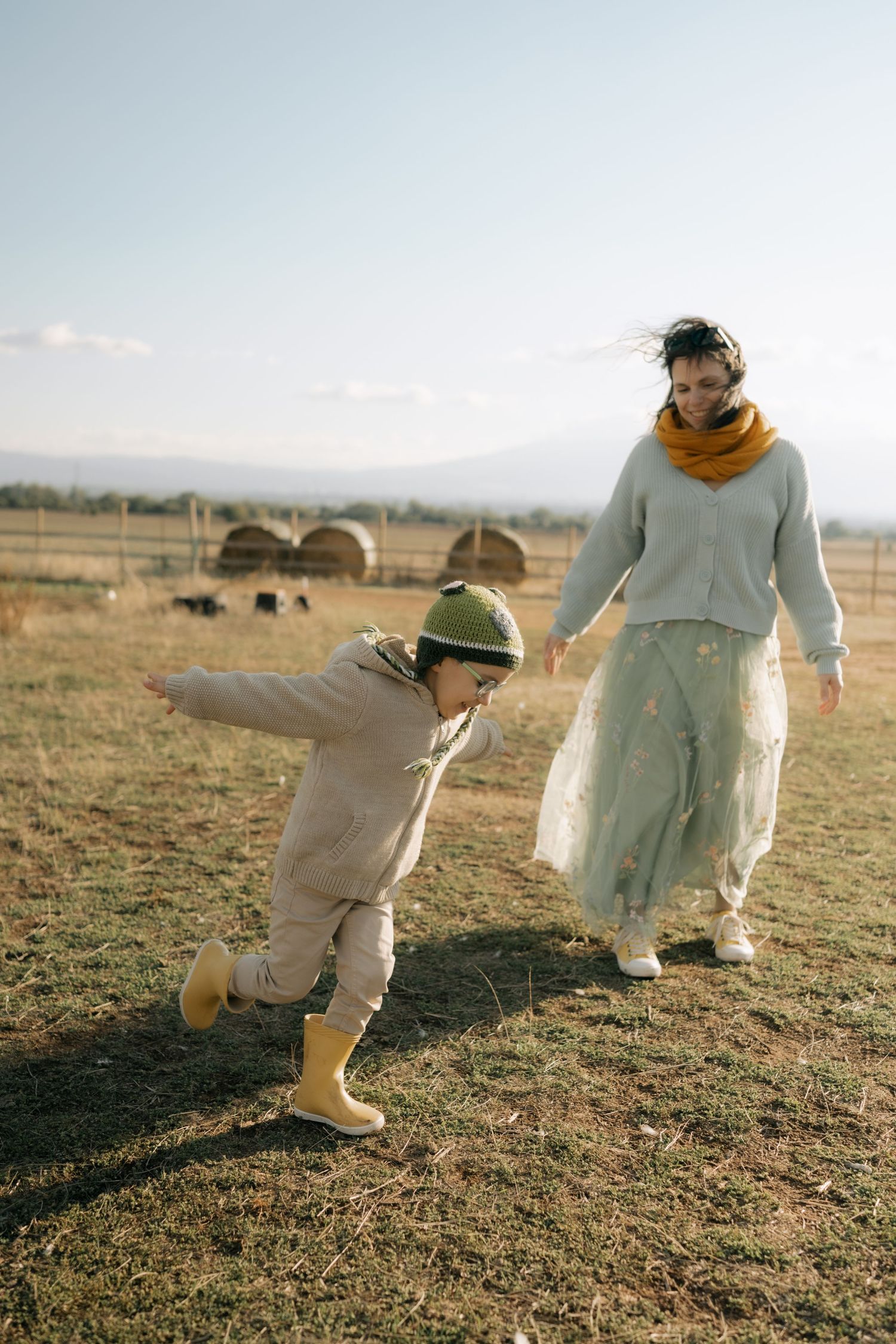 A person in a white dress and boots walks through a sunlit field at golden hour.