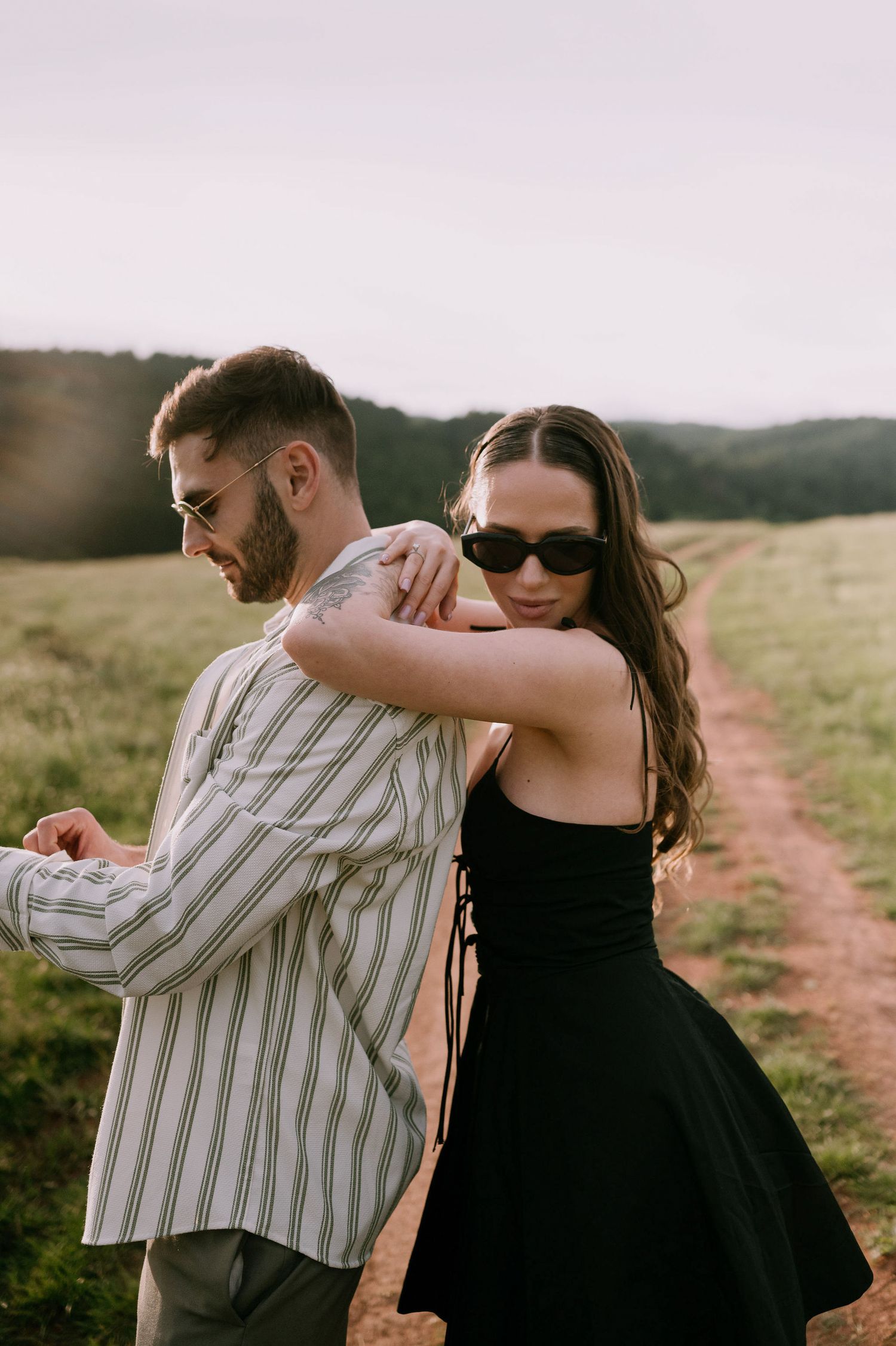 A couple dances together on a dirt path in a grassy field during golden hour.