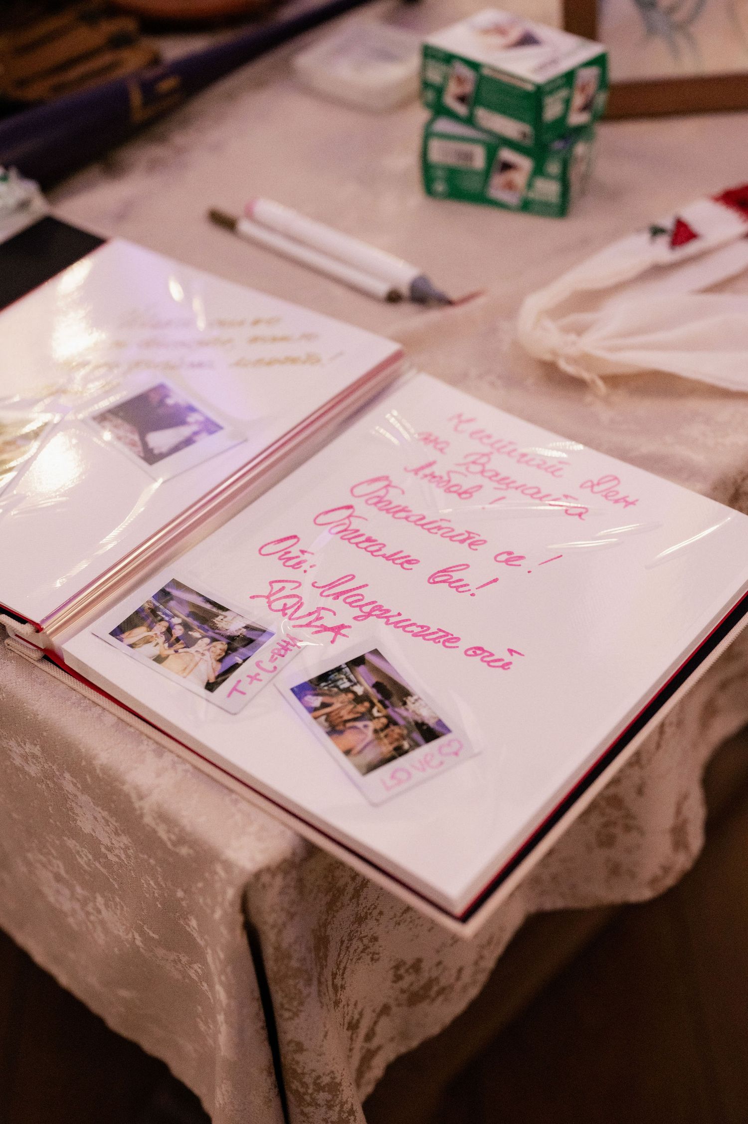 A wedding guest book with pink handwriting and polaroid photos lies open on a white tablecloth.