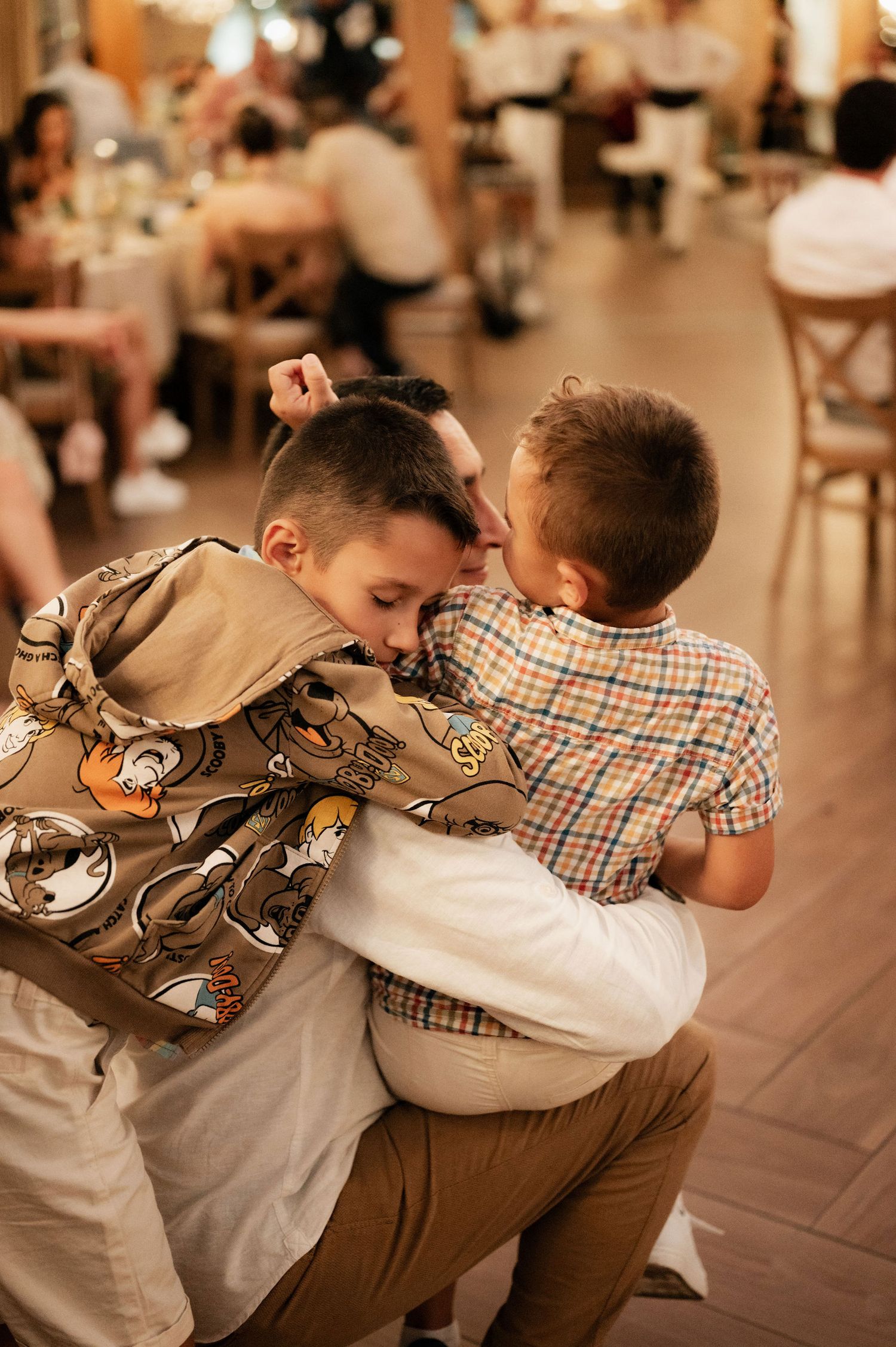 Two people share an emotional embrace on a dance floor at an indoor event with warm lighting.