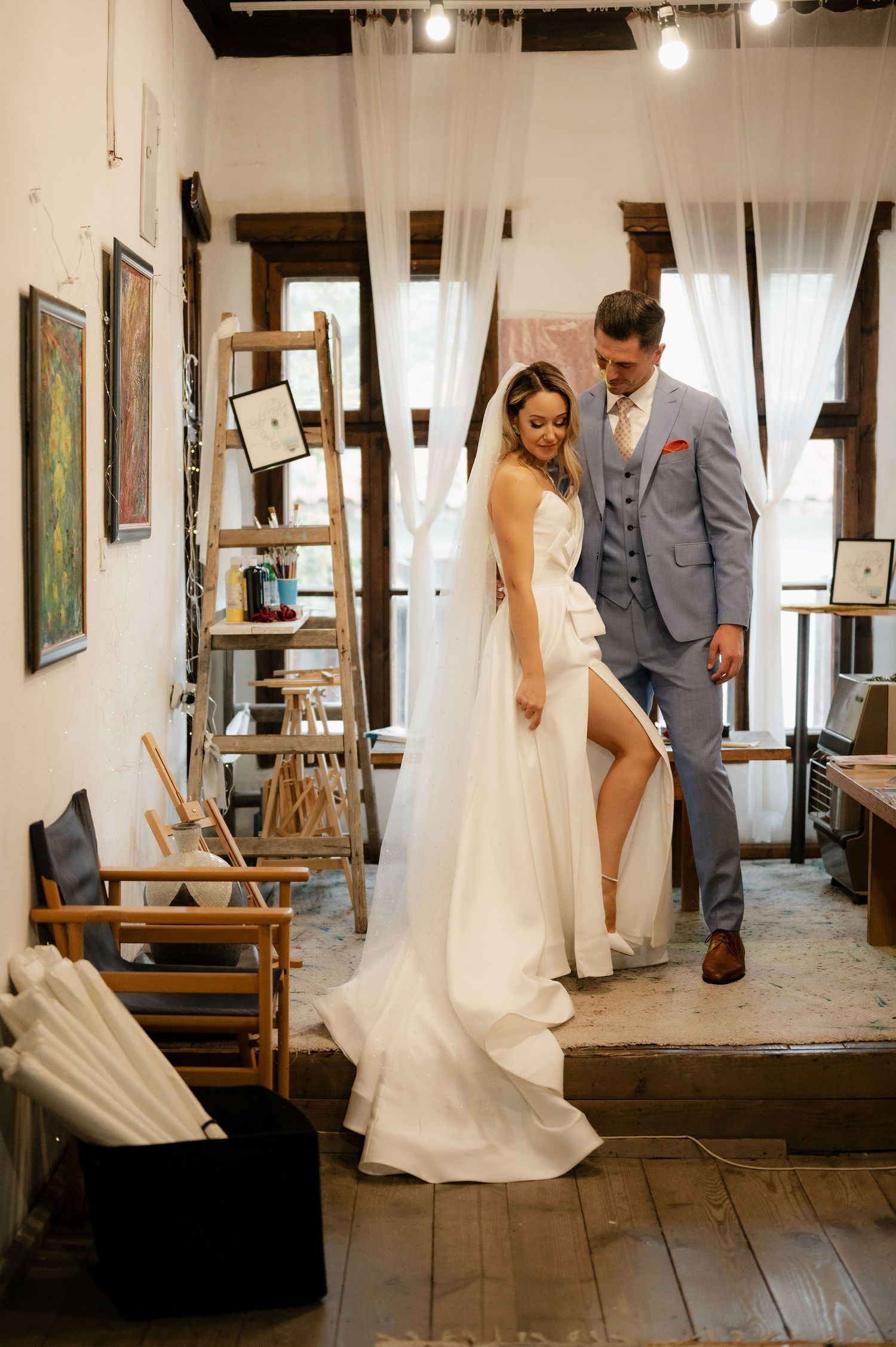 Wedding couple's first look photo series captured in a vintage room with wooden floors and white curtains.