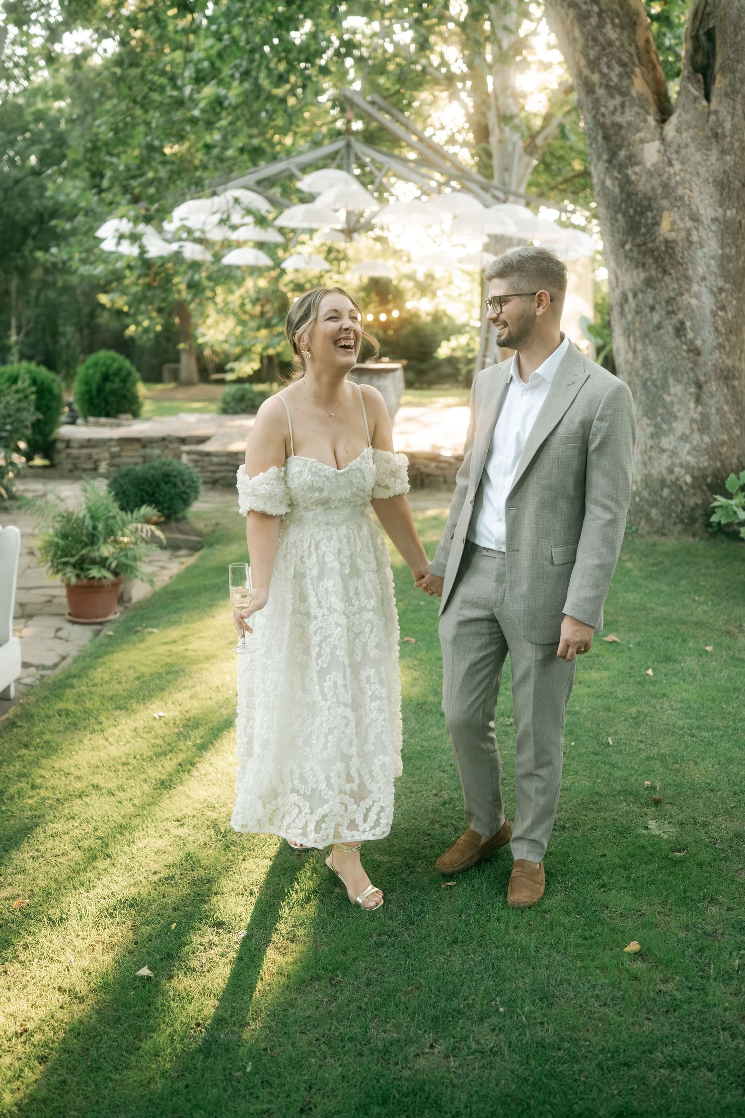 A couple walks hand in hand through a sunlit garden during a romantic outdoor photoshoot at golden hour.