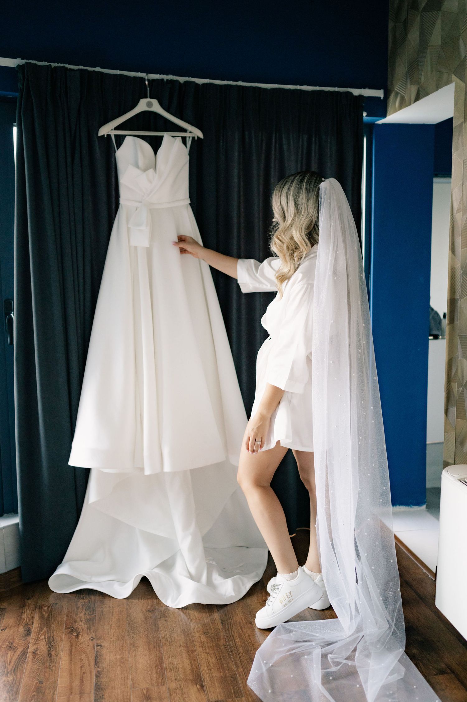 White wedding dresses hanging on display in a studio with dark curtains and wooden floors.